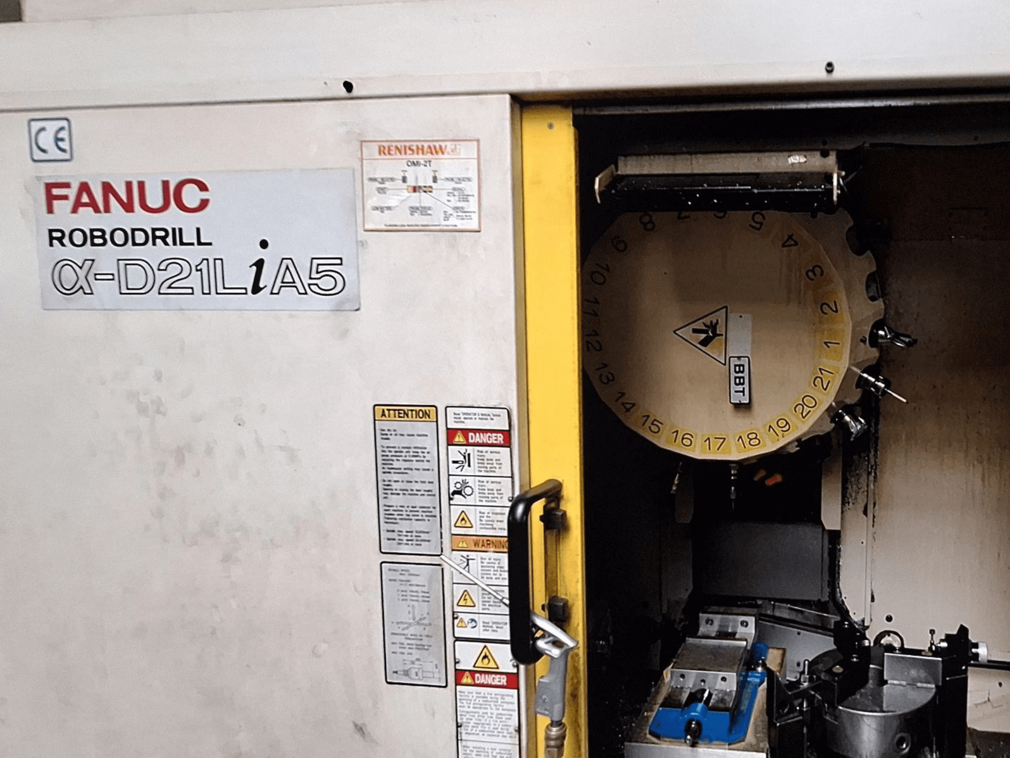 FANUC Robodrill α-D21LiA5, vue de face. Montre le carrousel d'outils et la zone d'usinage avec les pinces et les avertissements sur la porte.
