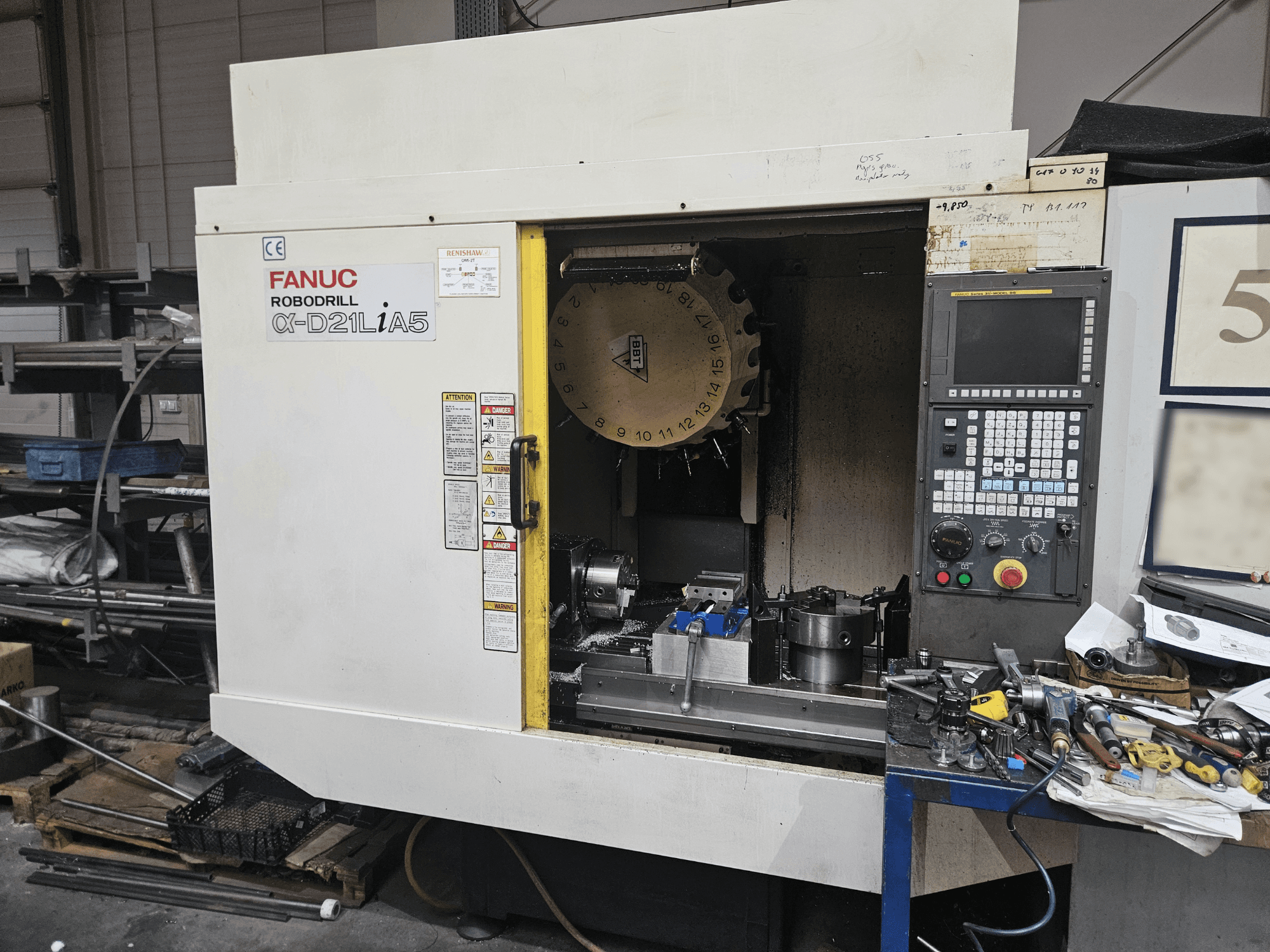 FANUC Robodrill α-D21LiA5, vue de face montrant le porte-outil et le panneau de commande, entouré d'outils et d'équipements dans un atelier.