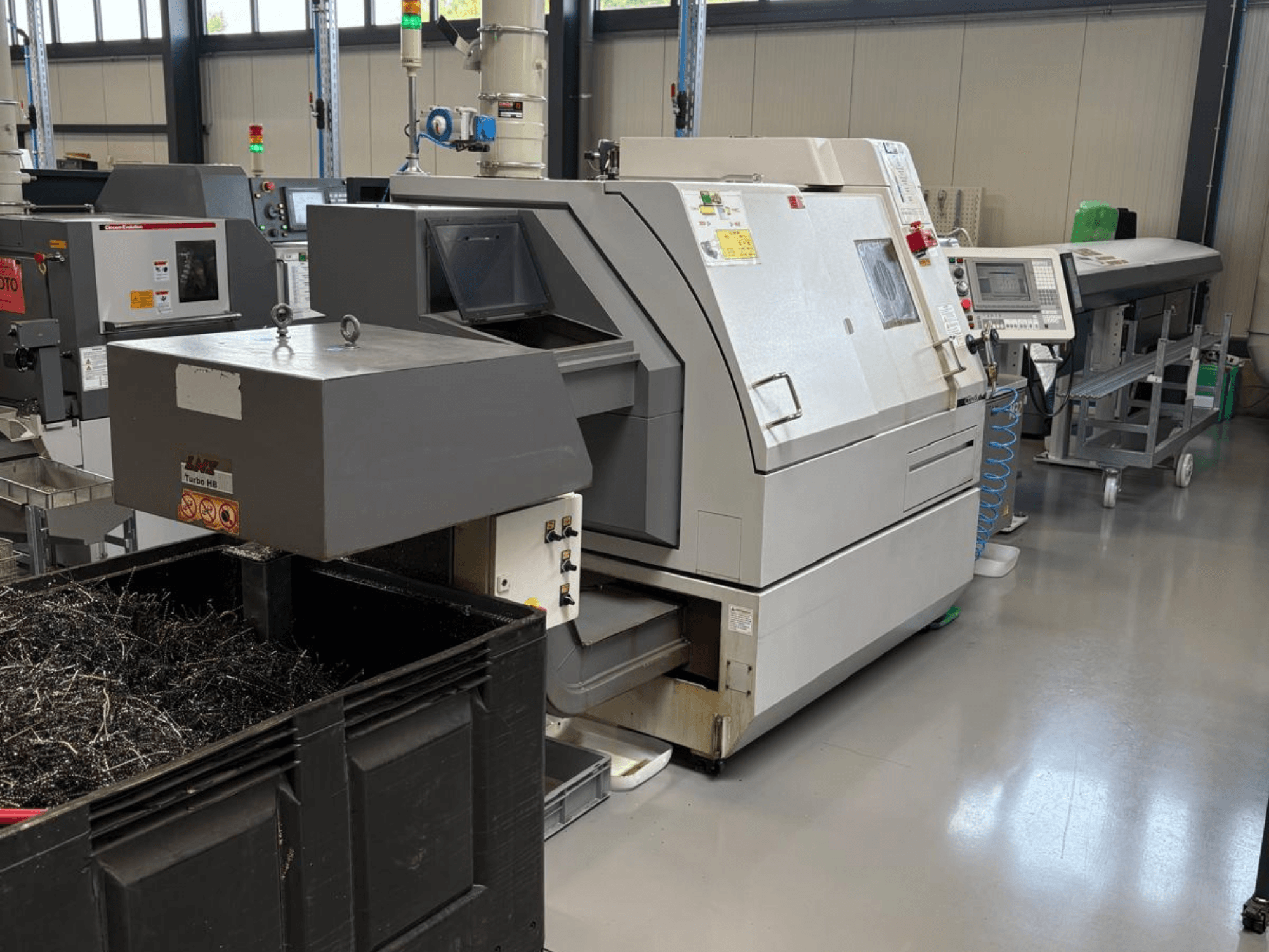 Machine industrielle LTA Turbo H8, vue de côté, avec un grand conteneur pour les copeaux de métal et le panneau de commande dans une usine.