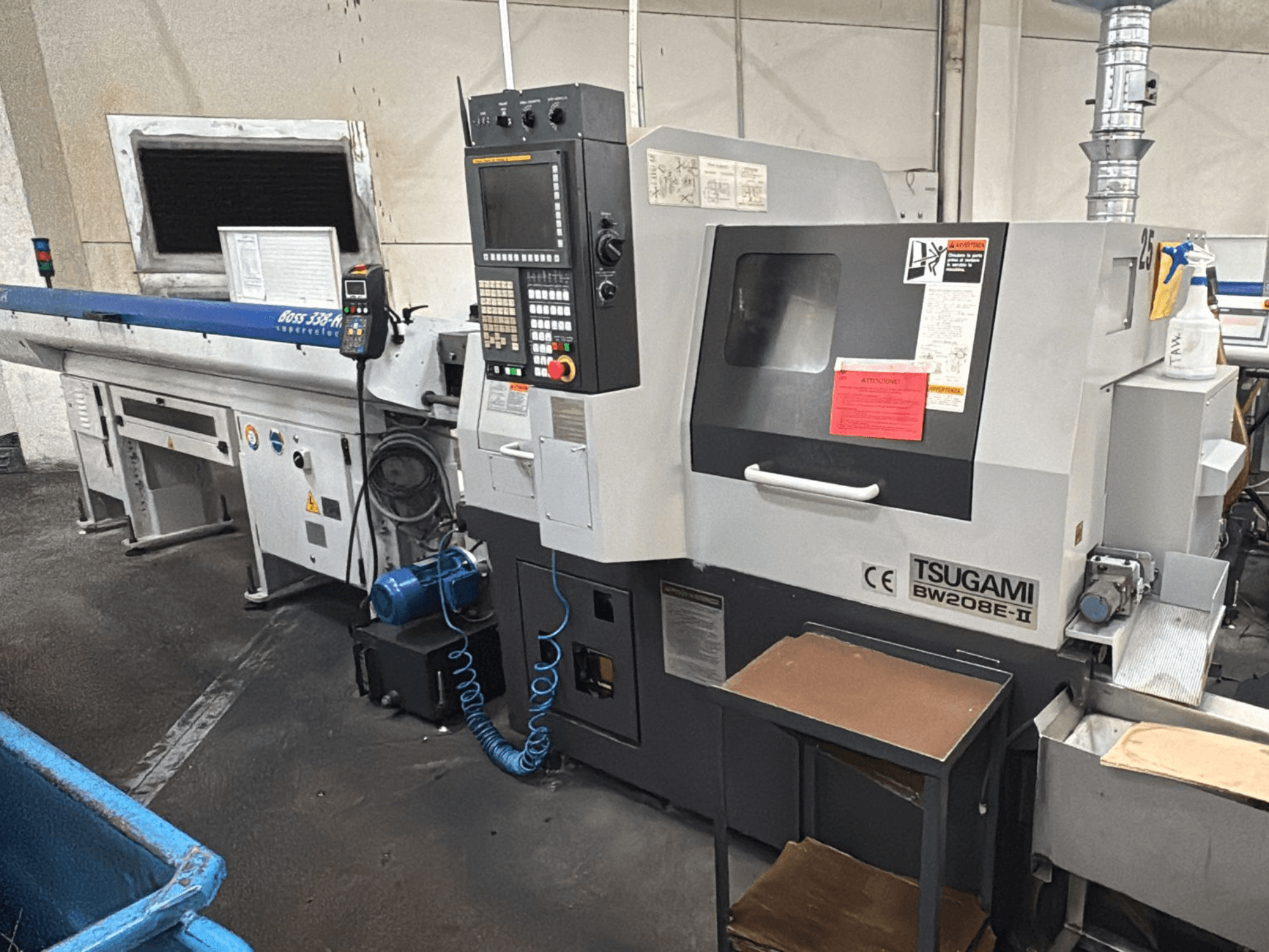 Machine CNC Tsugami BW208E-II dans un atelier, vue de face, avec le panneau de commande et les étiquettes de sécurité visibles.