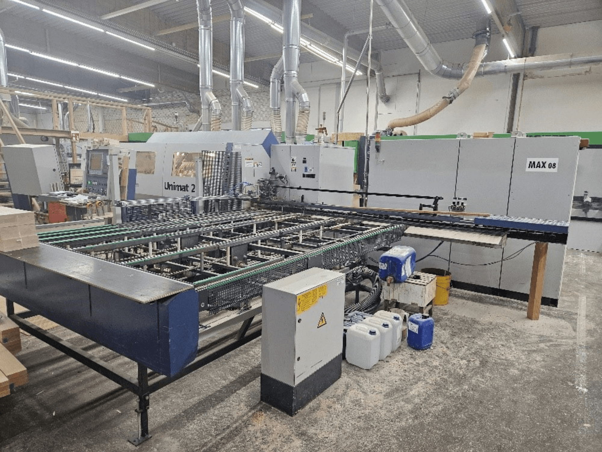 Vue latérale d'une machine CNC Unimat 2 dans un atelier, avec des bandes transporteuses et des composants techniques avec l'unité Max 08 visible.