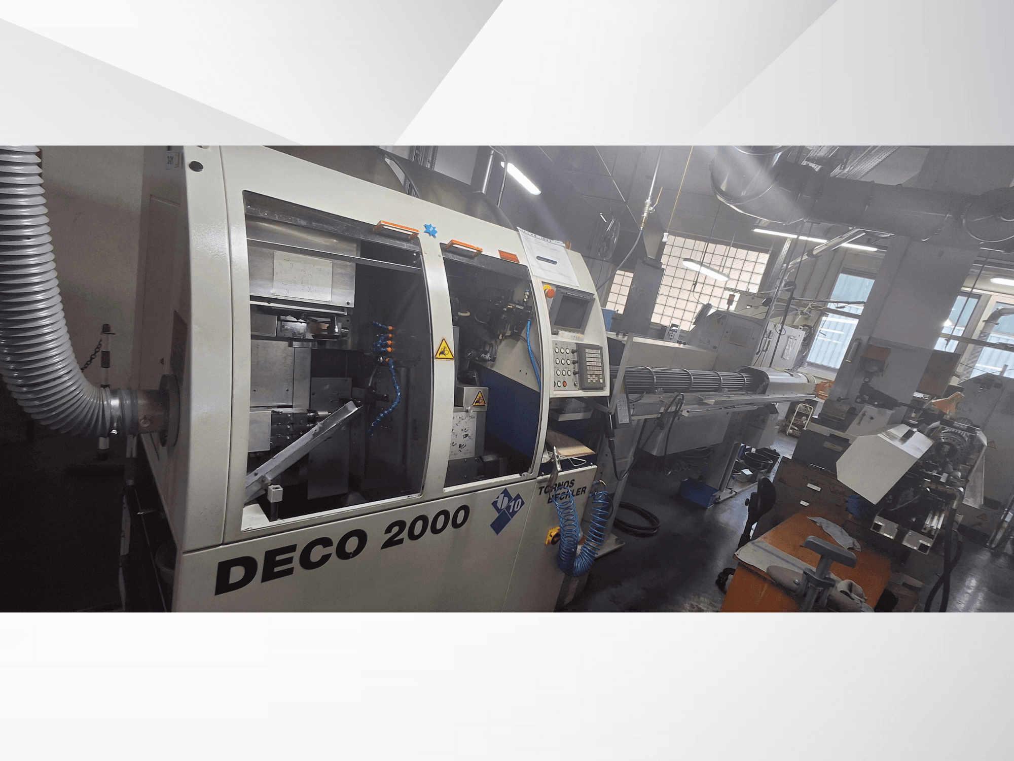 Machine CNC DECO 2000 dans un atelier, vue de face, montrant les commandes et un montage de pièces longues à droite.