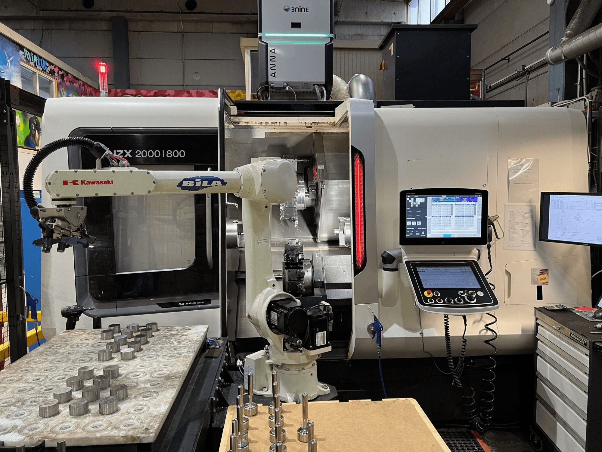 Tour horizontal DMG MORI NZX 2000/800SY dans un atelier, avec le bras robotisé Kawasaki et les commandes bien visibles.