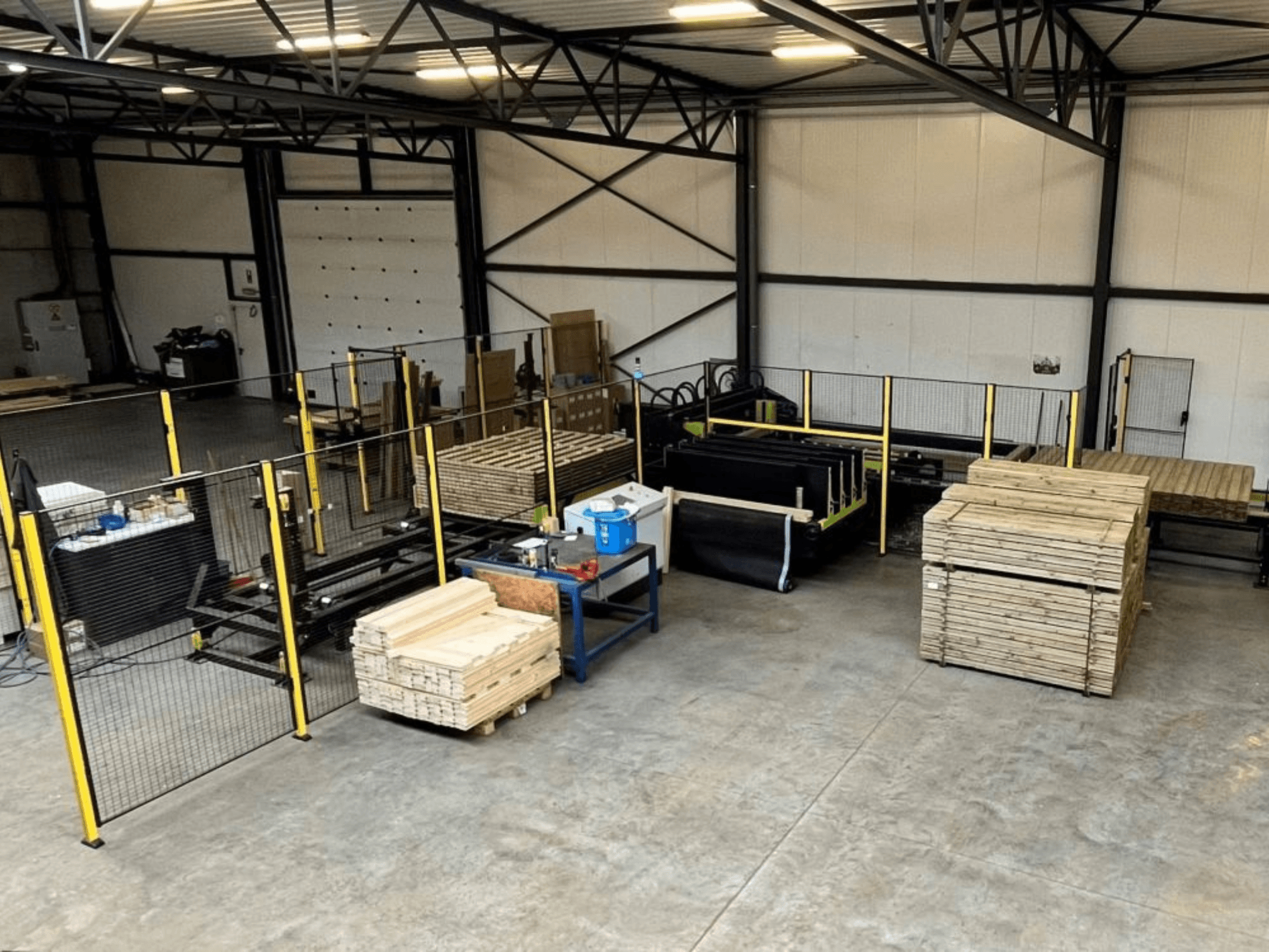 Ligne de production complète (ISM ATM-01) pour le bois, vue d'en haut, montrant des machines, des palettes en bois et des clôtures de sécurité.