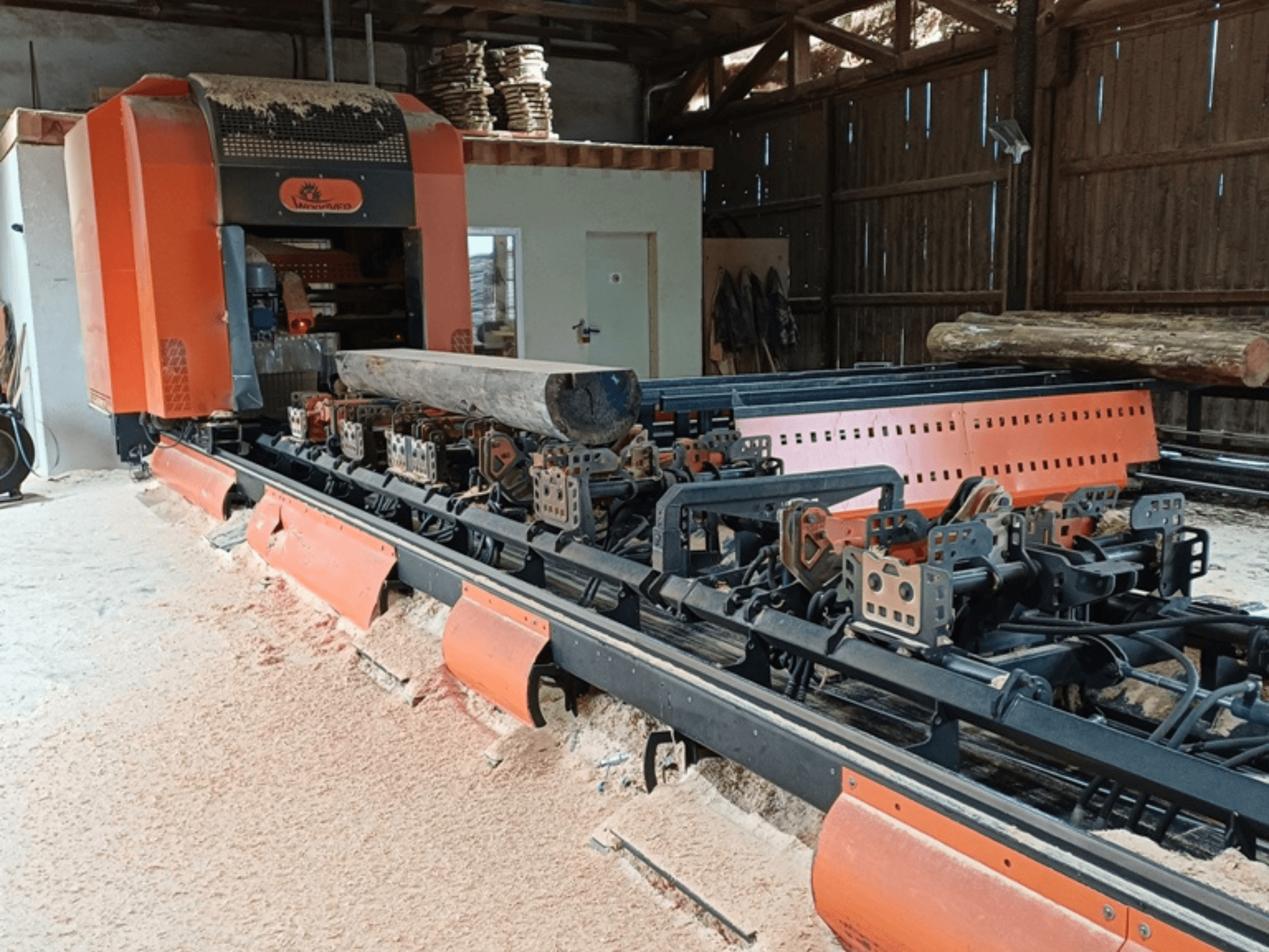 Fraiseuse à bois orange avec une grume positionnée sur le convoyeur, vue de face dans un atelier.