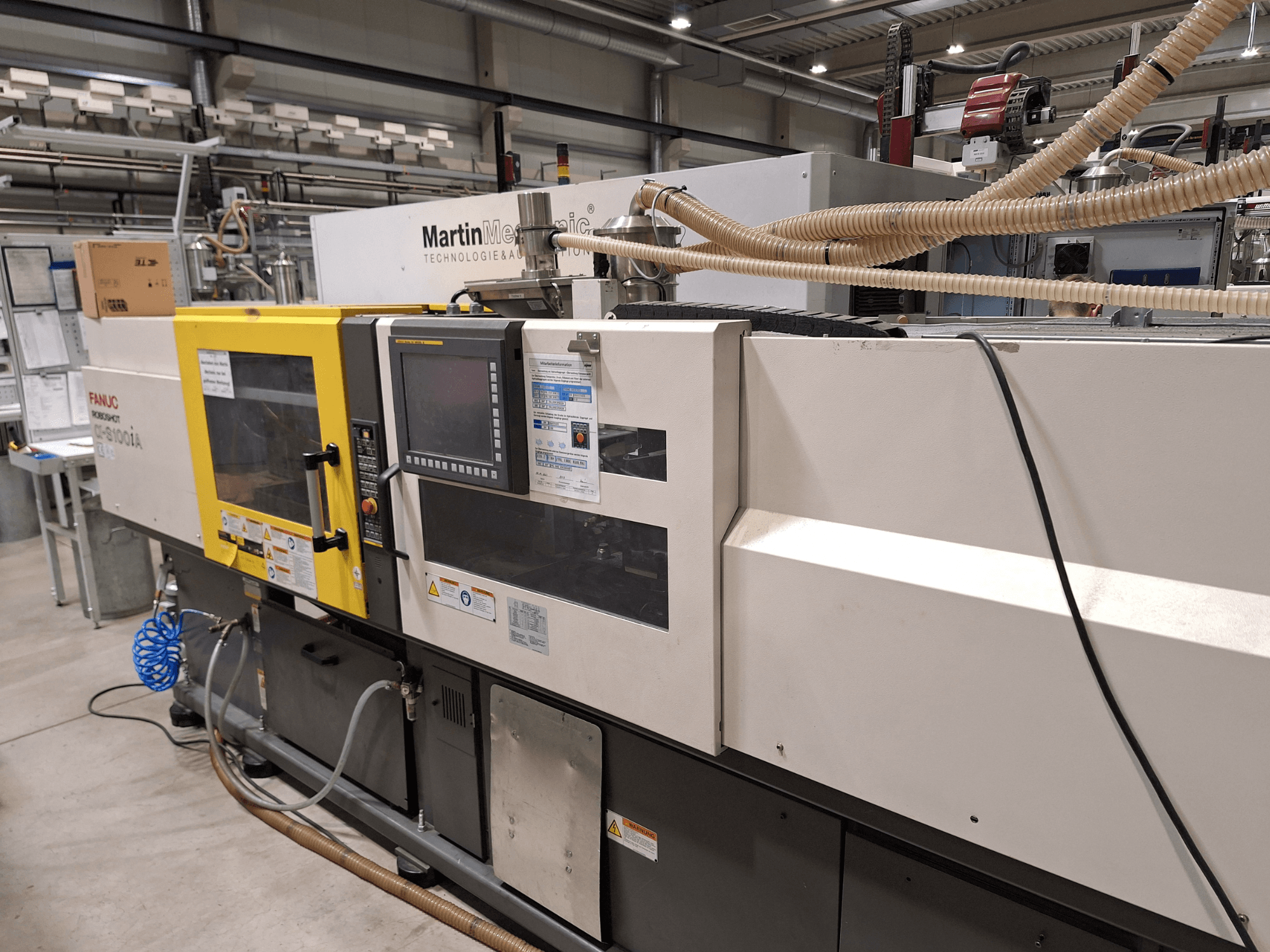 Machine à injecter électrique FANUC Roboshot S100iA, vue latérale, équipée d'un écran tactile et d'étiquettes de sécurité.