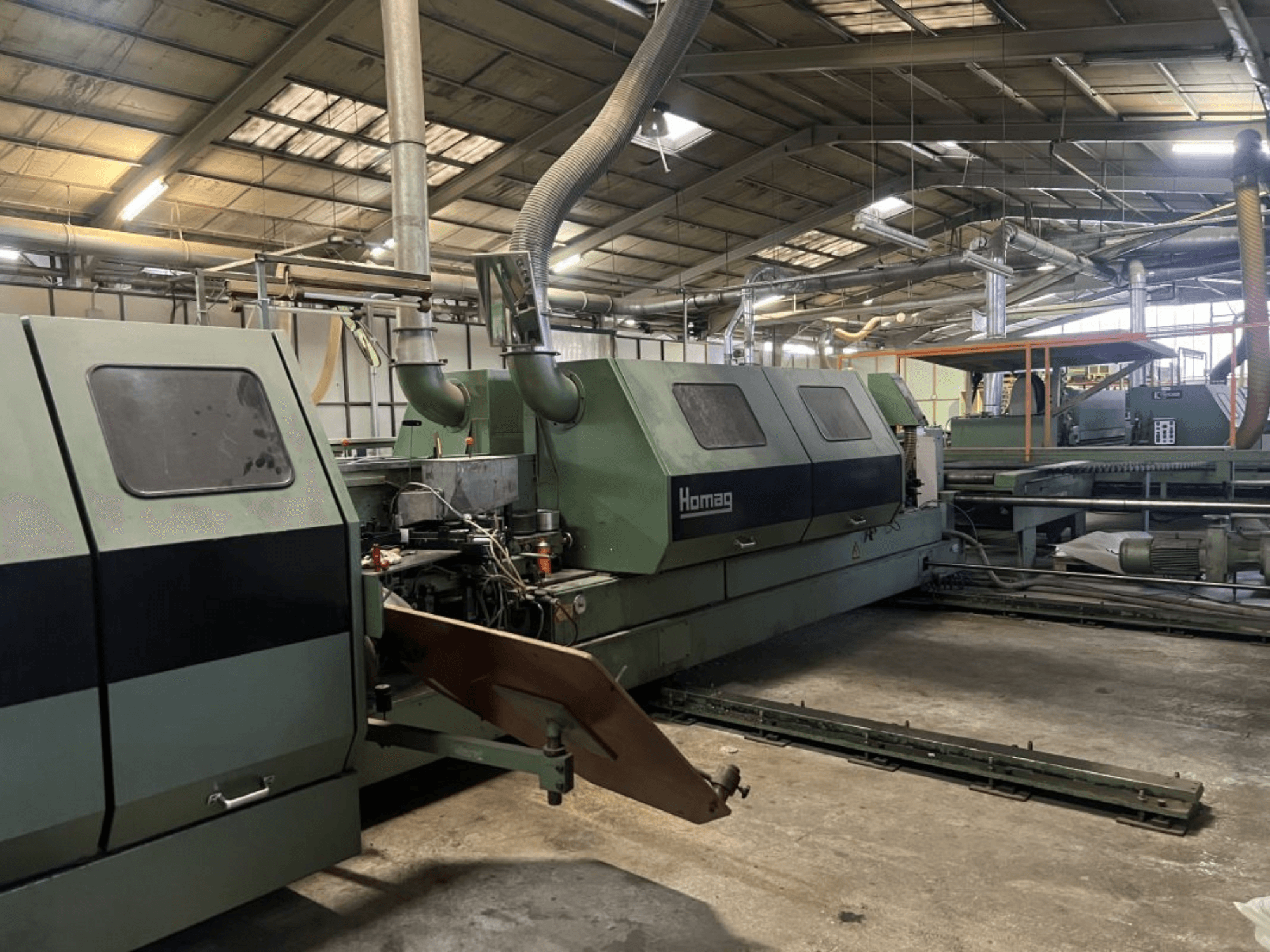 Machine industrielle Homag en vert, vue de côté, avec les composants opérationnels et le panneau de commande visibles dans un entrepôt.