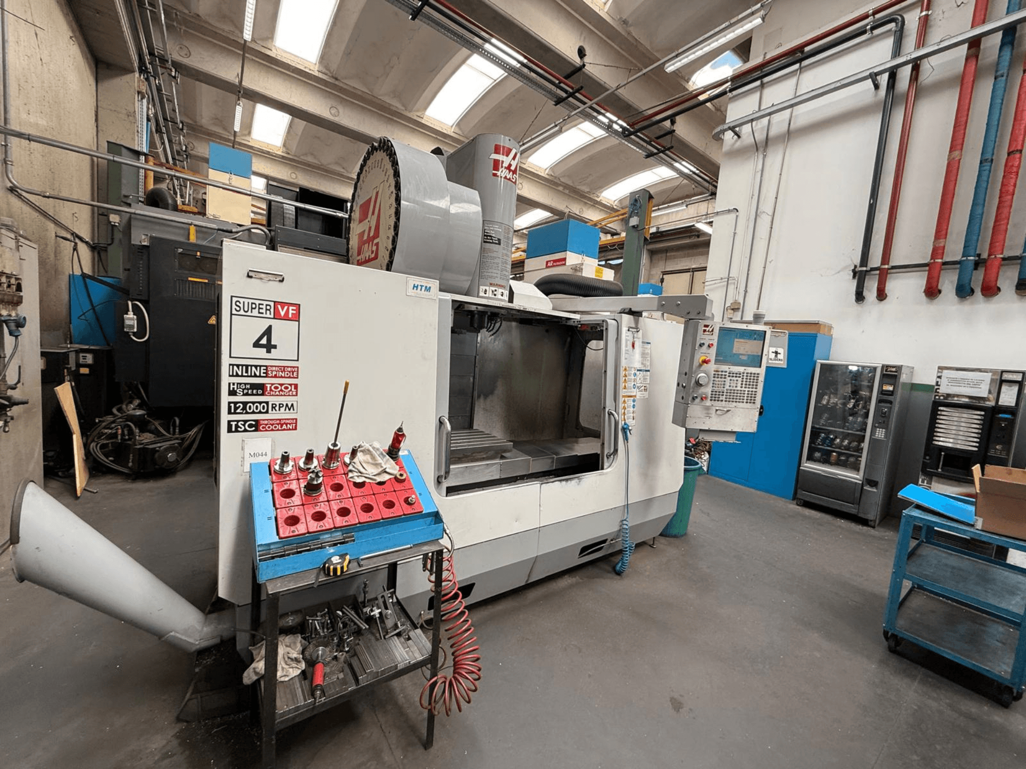 Fraiseuse CNC HAAS Super VF 4 avec panneau de commande, broche de 12 000 tr/min et outils sur un support de rangement bleu, vue de côté.