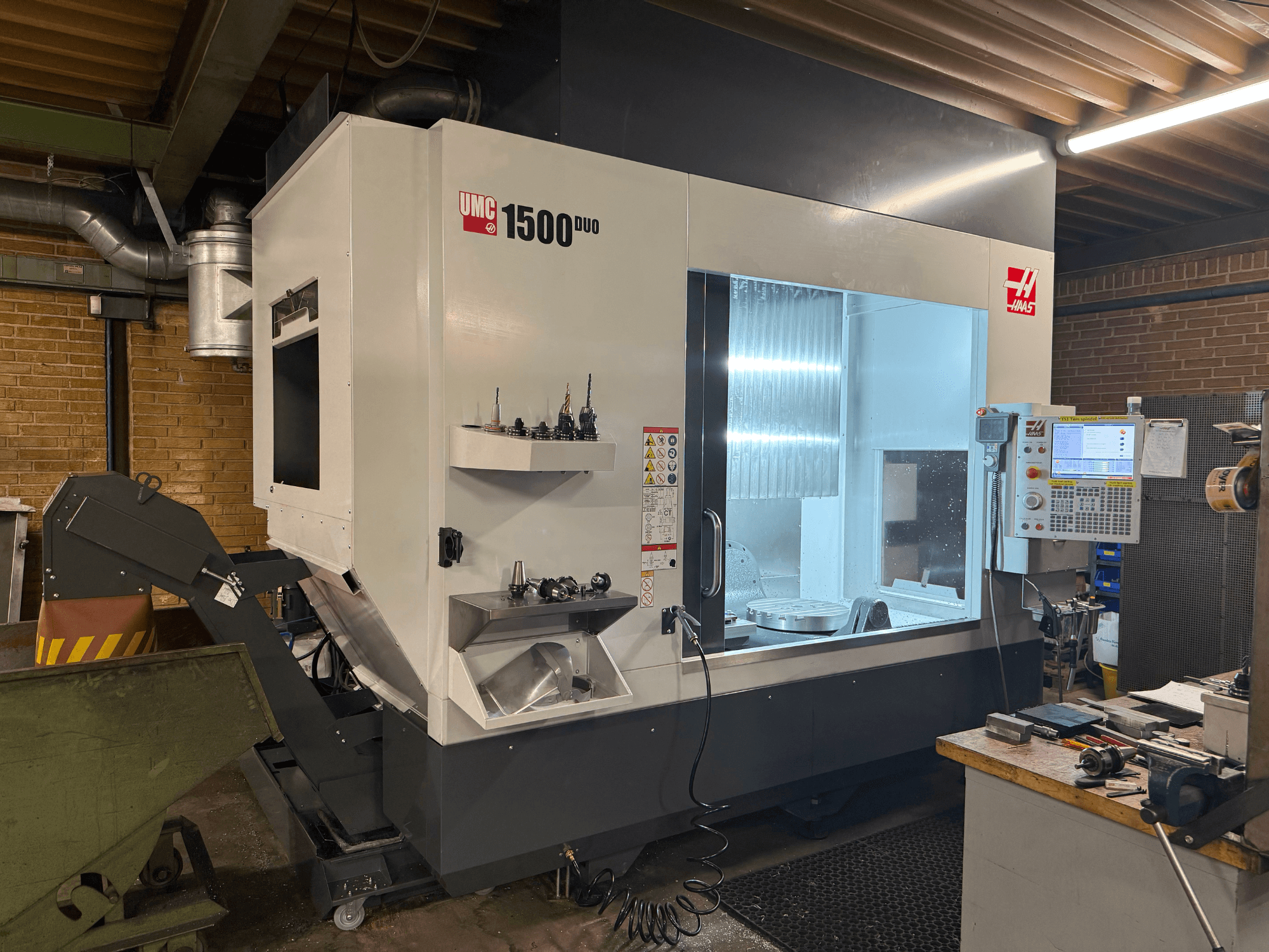Machine CNC Haas UMC 1500DUO, vue de face, avec une grande fenêtre, un panneau de commande et des porte-outils sur une étagère.