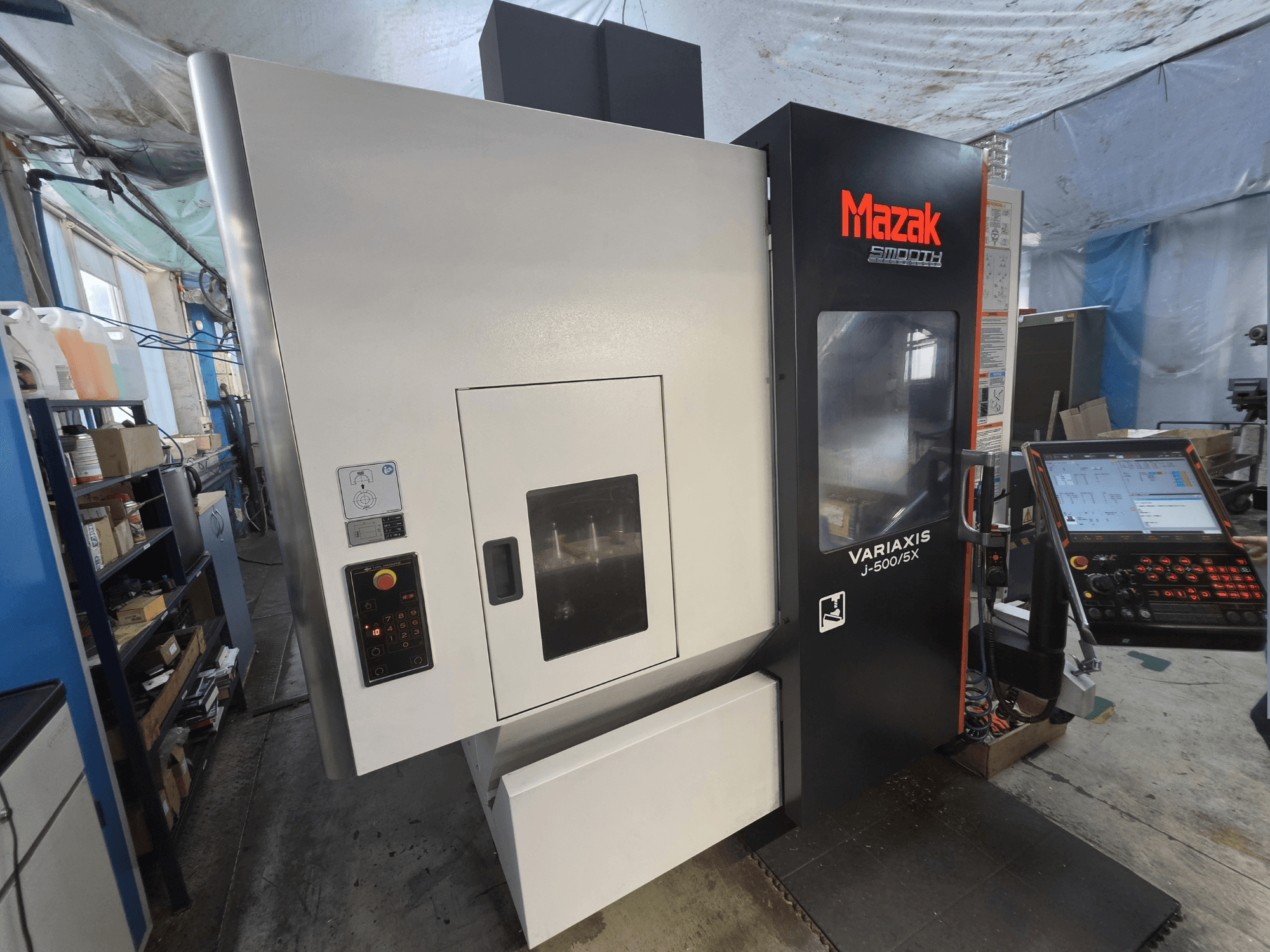 Centre d'usinage vertical Mazak VARIAXIS J-500/5X vu de face, doté d'un panneau de commande et d'une grande baie vitrée donnant sur la zone d'usinage.