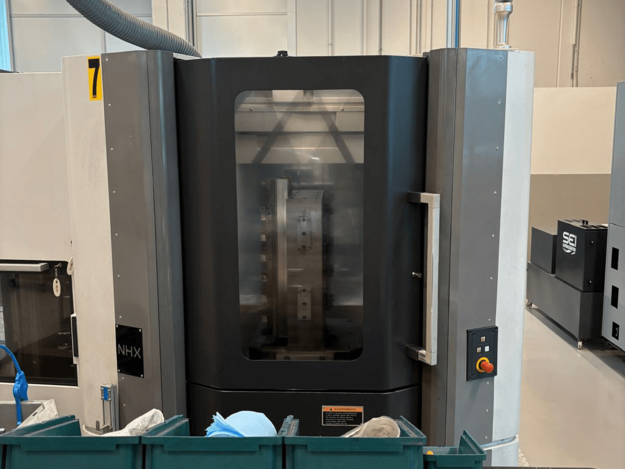 Machine CNC NHX vue de face, montrant le panneau de commande et l'affichage clair ; située dans un atelier avec des bacs verts à proximité.