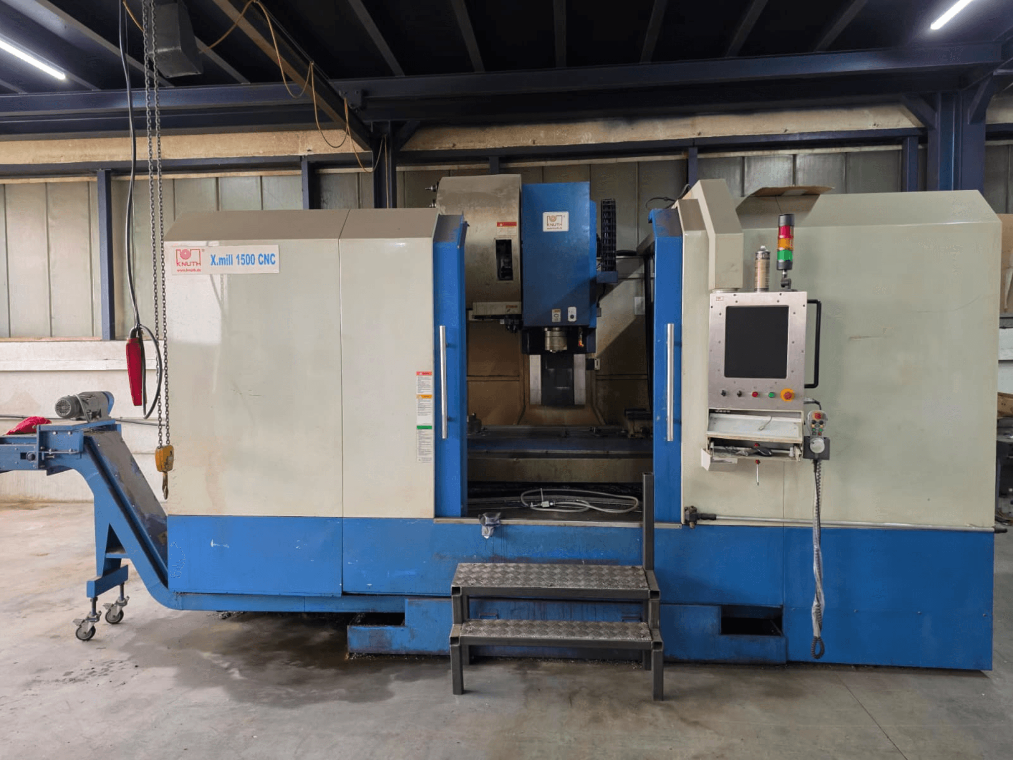 Centre d'usinage vertical CNC KNUTH X-MILL 1500, vue de profil, avec panneau de commande, marches et convoyeur de sortie.