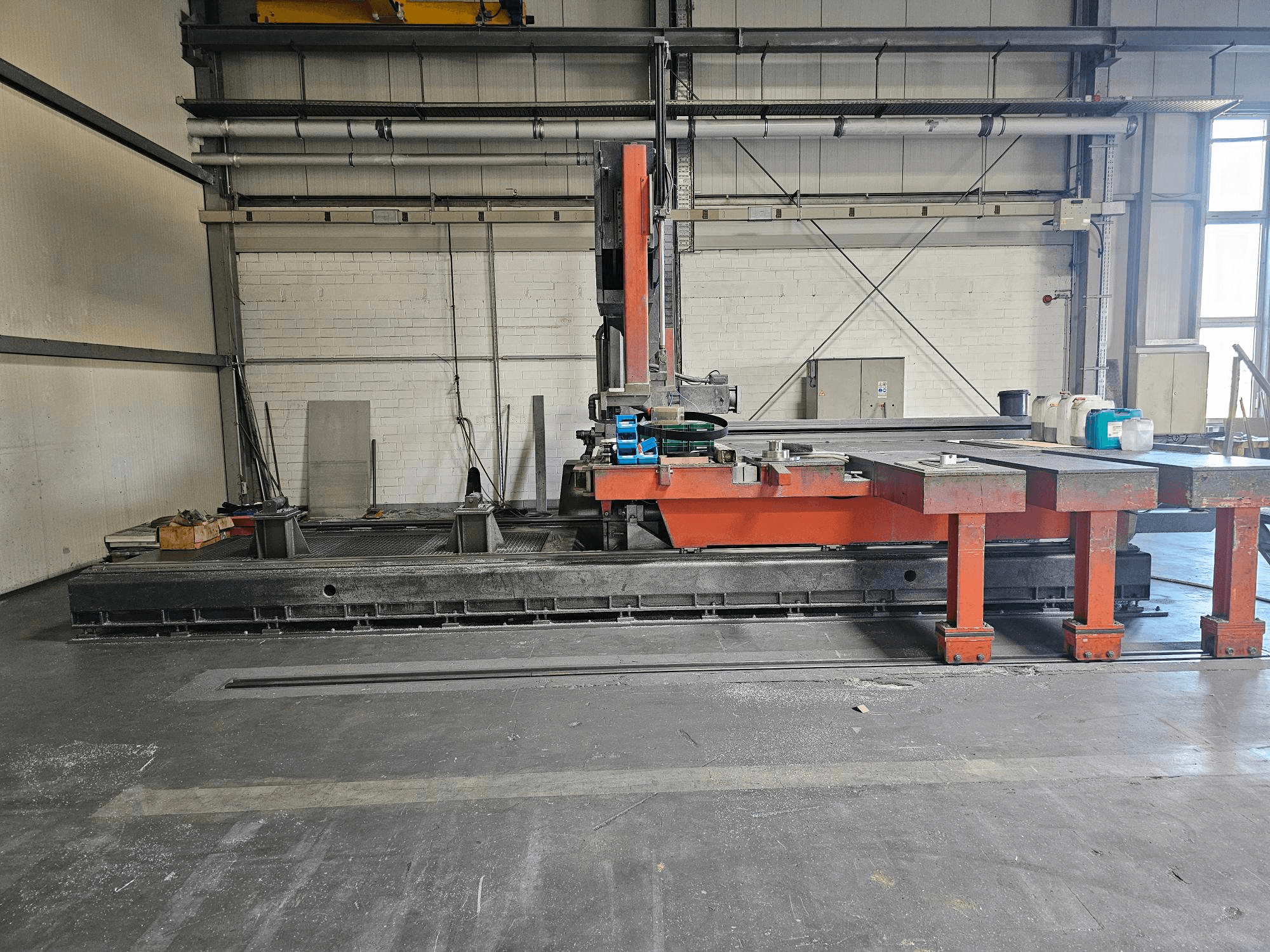 Machine à découper industrielle dans un atelier ouvert, orange et noir, avec une grande table ; vue latérale montrant les accessoires et l'espace de travail.
