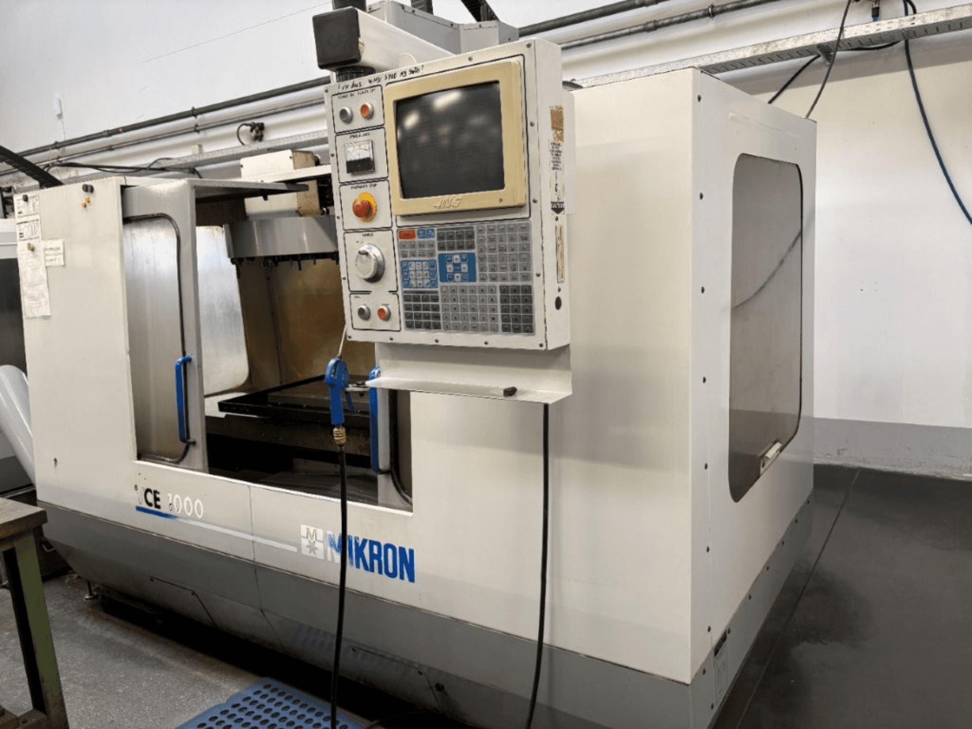 Machine CNC Mikron CE 2000, vue de face ; panneau de commande avec boutons et écran, extérieur argenté et zone de travail.