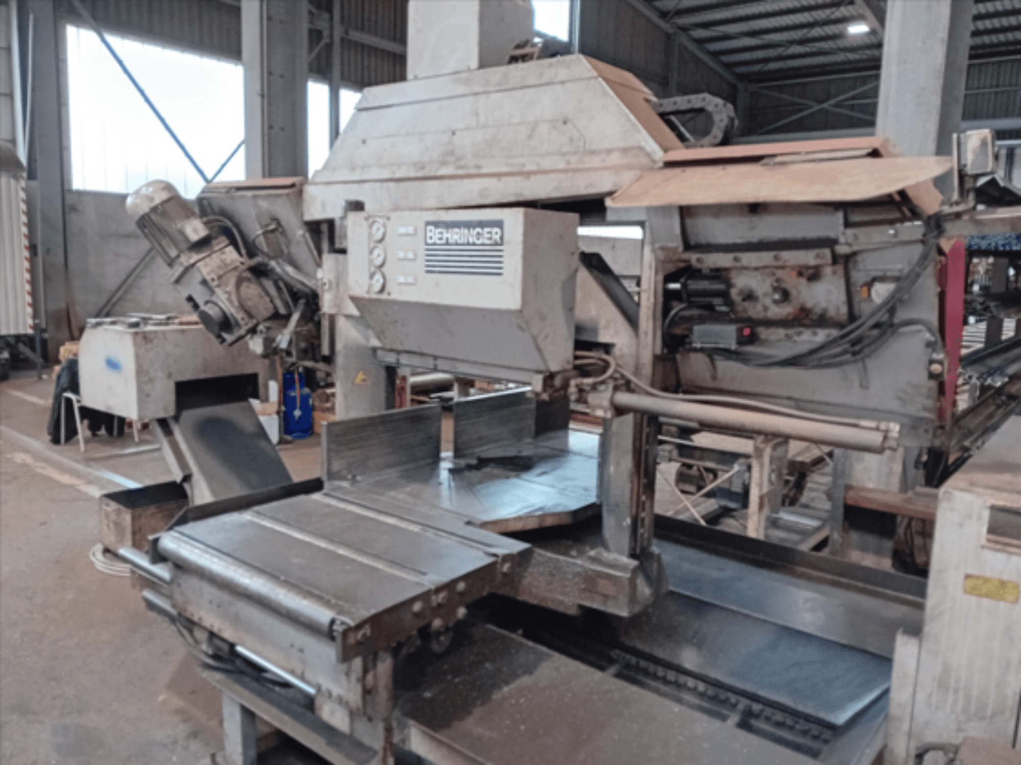 La scie à ruban Behringer, vue de face, est équipée d'une grande lame, d'un moteur et d'une table réglable. Elle est idéale pour le découpage des métaux dans un atelier.