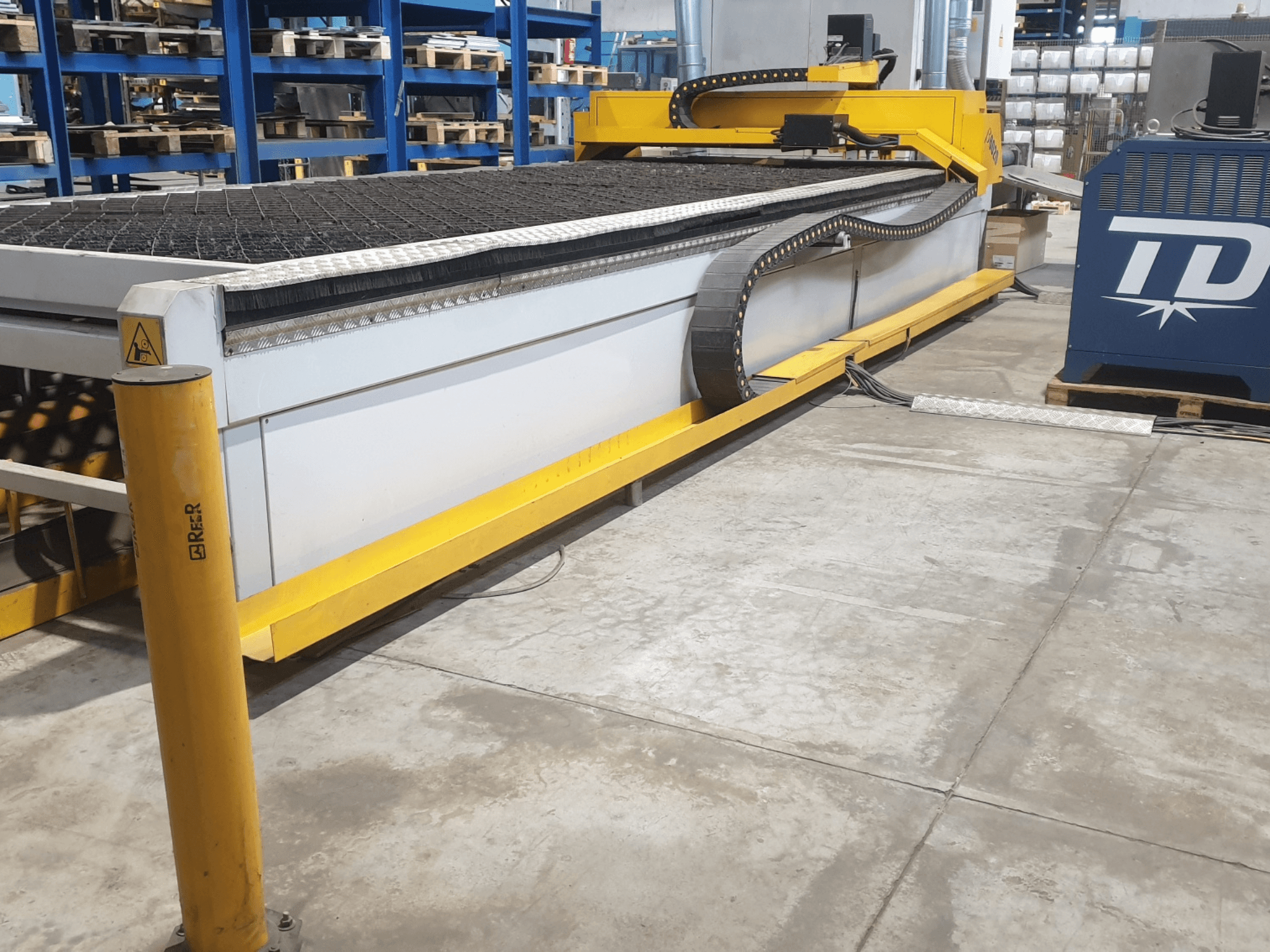 Machine à découper industrielle avec garniture jaune, vue de face, comportant un banc texturé et un panneau de commande, placée sur le sol d'une usine.