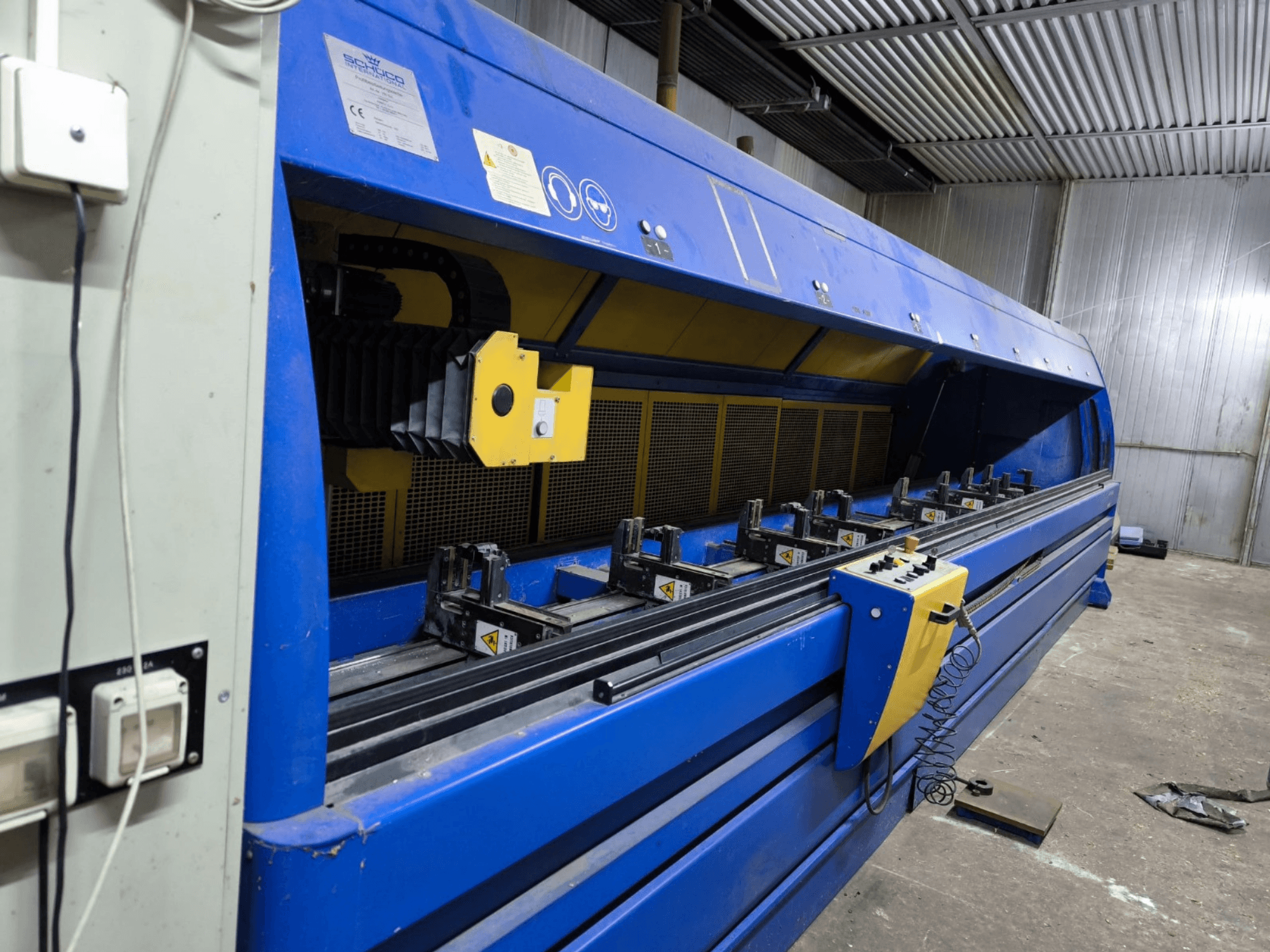 Machine de découpe industrielle Schneider en bleu, vue de côté, avec le panneau de commande, les courroies et les multiples stations de serrage visibles.