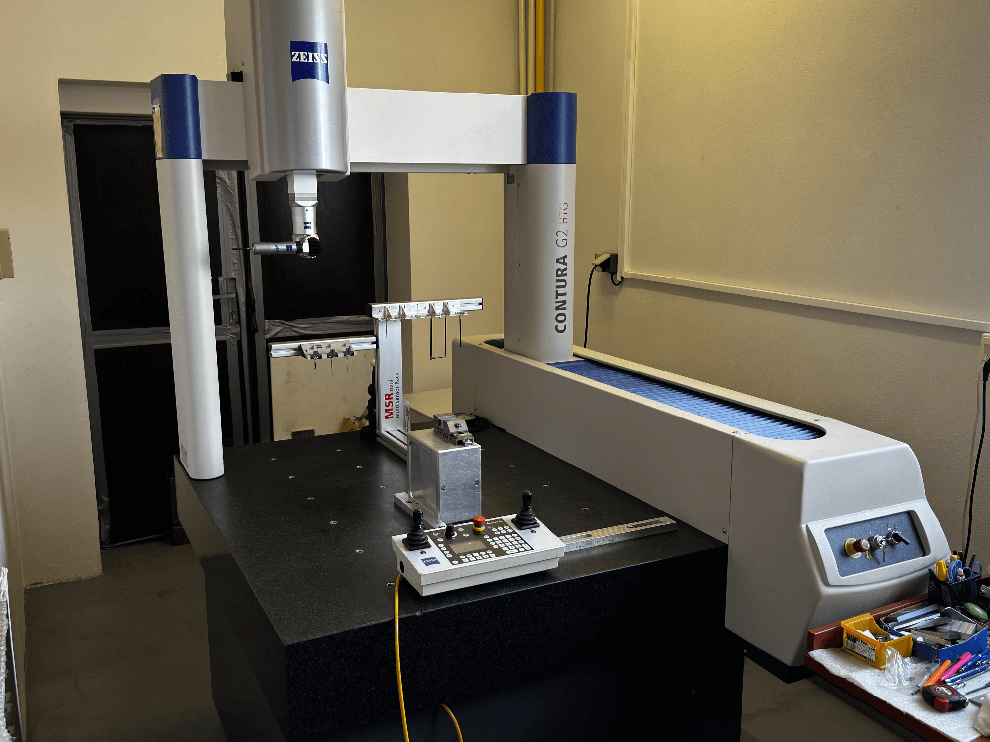 MMT ZEISS Contura G2 dans un laboratoire, vue de face montrant le bras de mesure, le panneau de commande et l'espace de travail adjacent.
