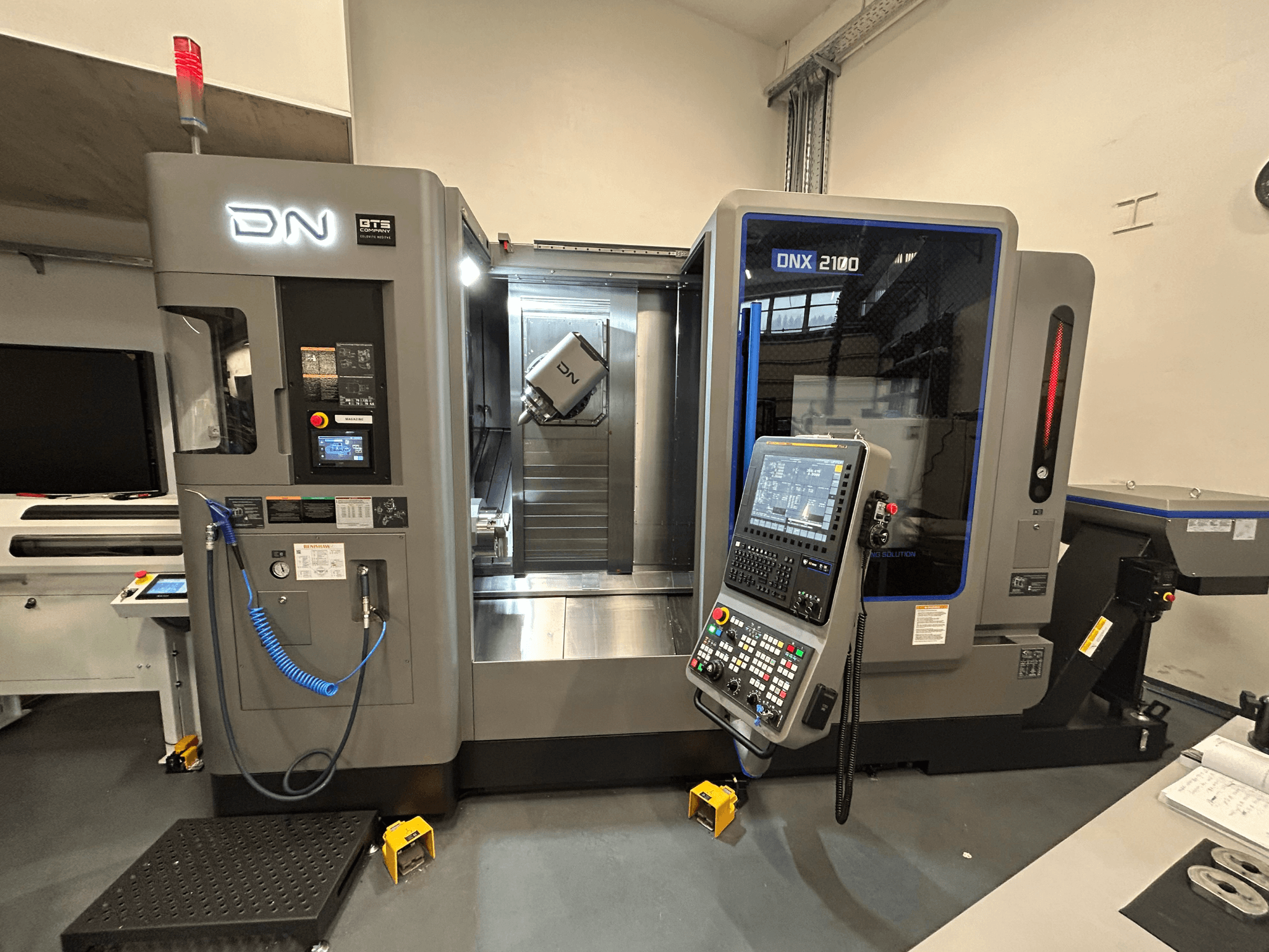Machine CNC DN ONX 2100, vue de face, comprenant le panneau de commande, la zone de travail et l'outil. Equipée d'un éclairage de sécurité et d'indicateurs de fonctionnement.