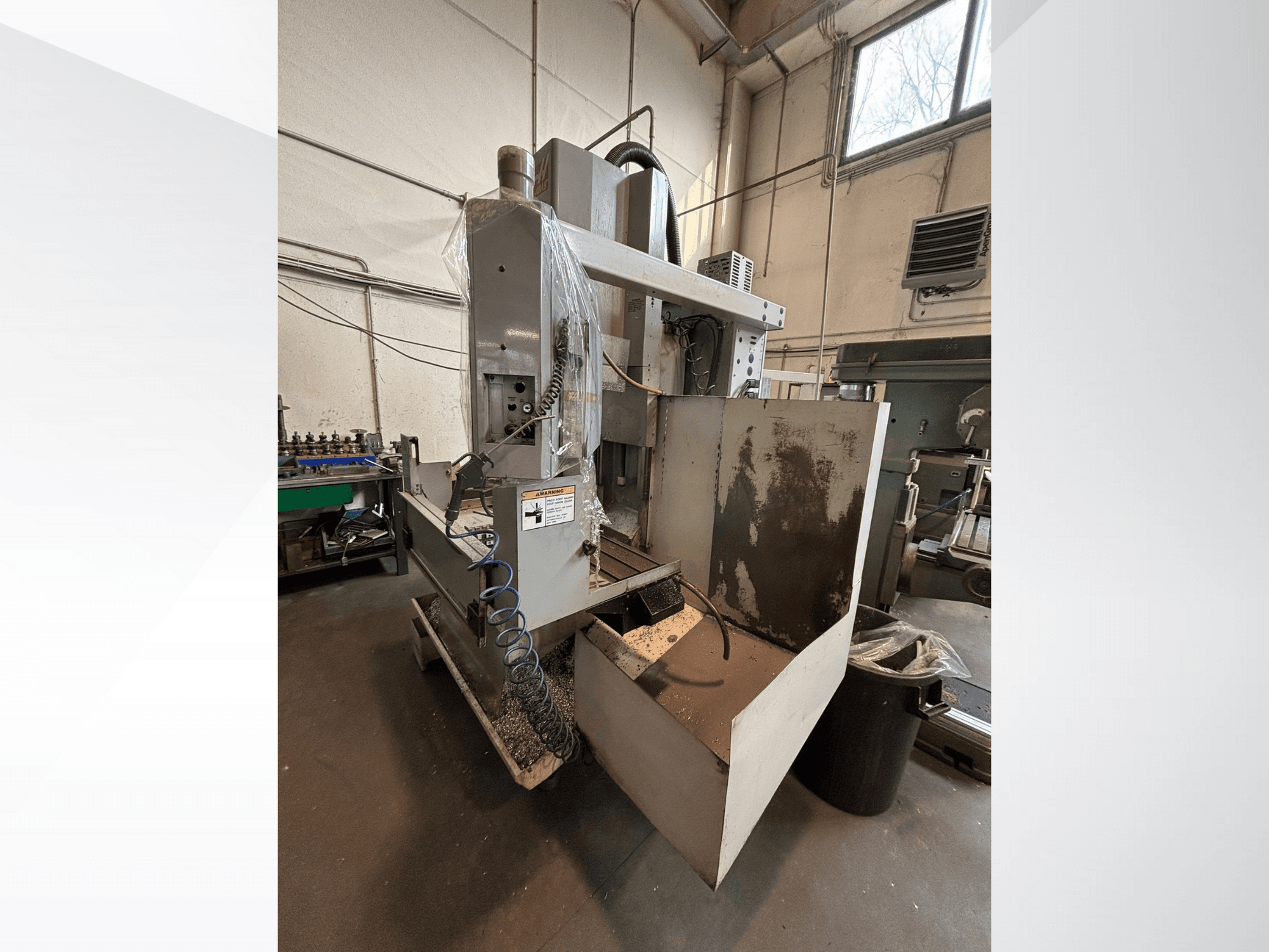 Fraiseuse verticale avec capot de protection, vue latérale ; comprend le tuyau d'arrosage et le panneau de commande visible. Idéale pour l'usinage.