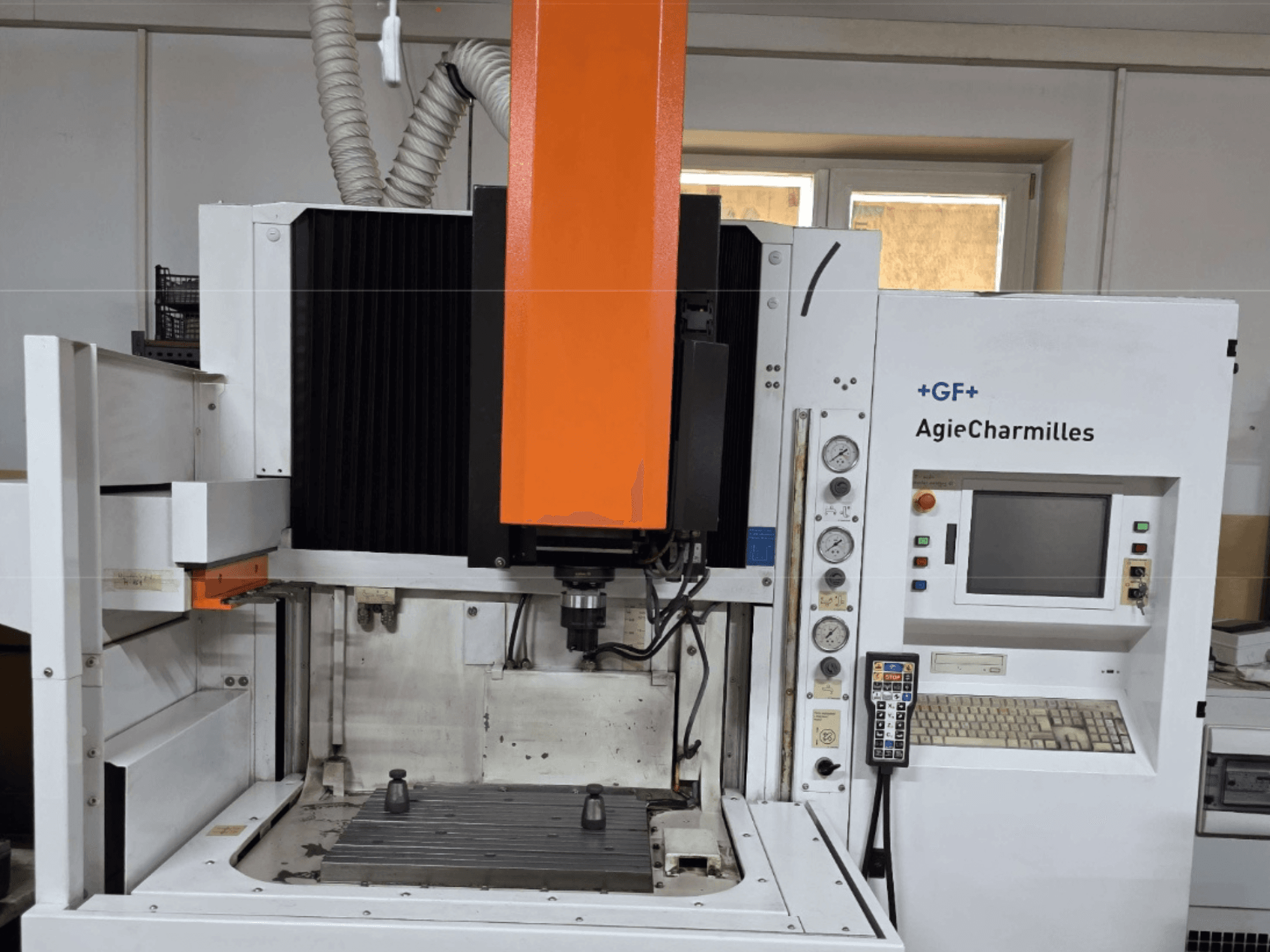 Centre d'usinage AgieCharmilles vu de face avec une grande broche orange, un panneau de commande et une table de travail visible.