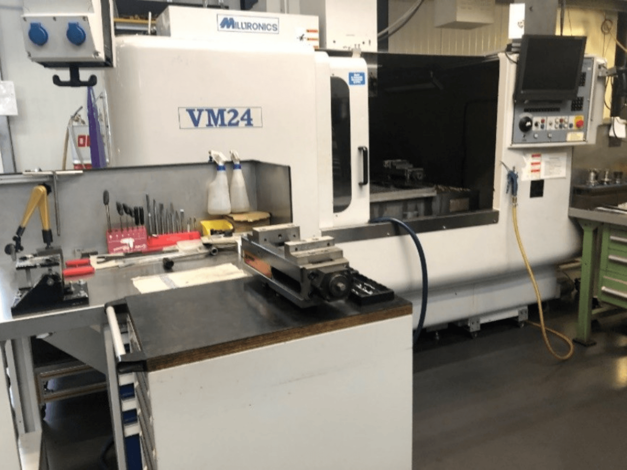 Espace de travail avec la machine CNC Milltronics VM24. Vue de face avec des outils et des équipements sur un établi.