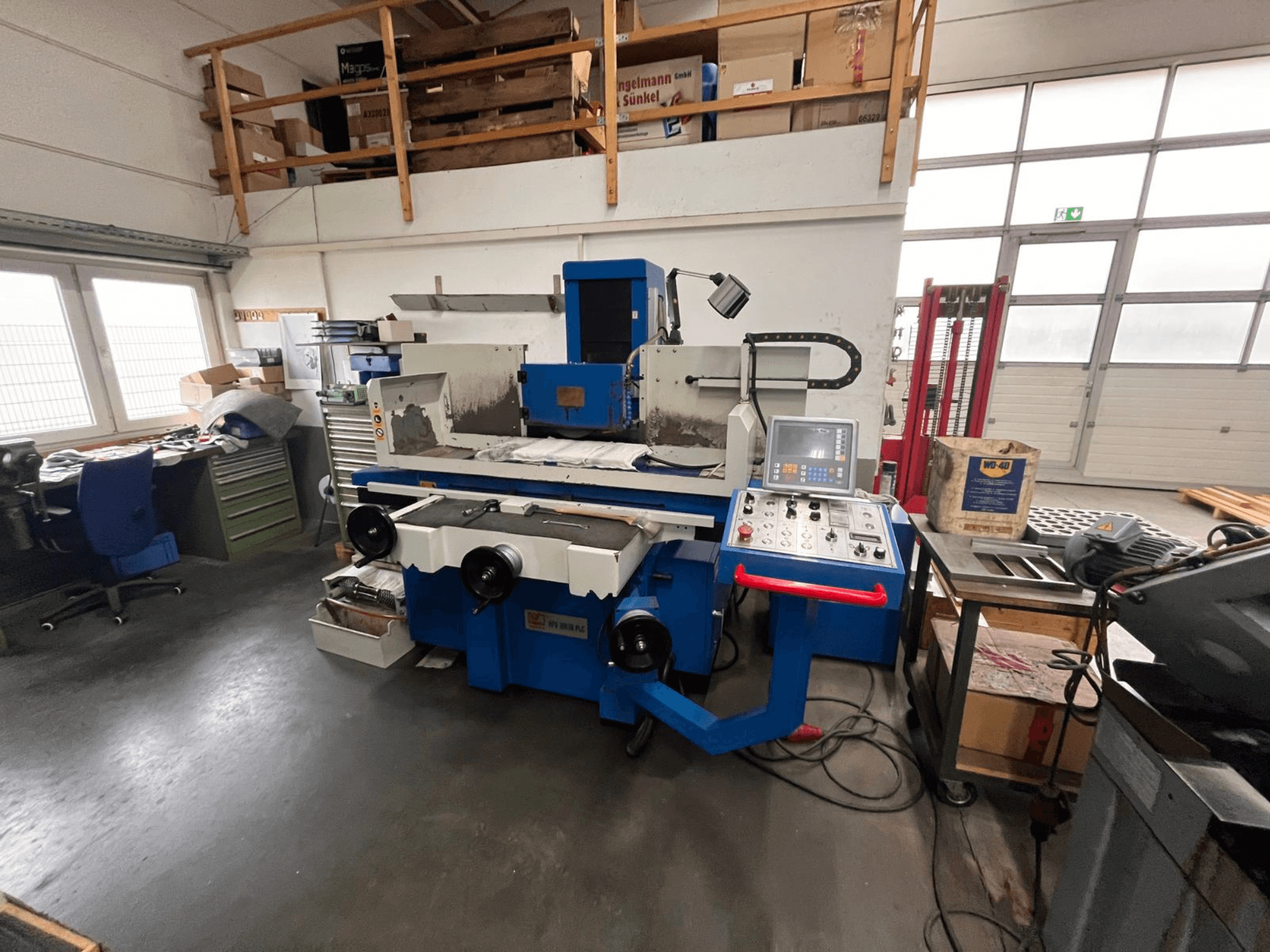 Meuleuse de surface bleue avec panneau de commande numérique, vue de face, montrant l'encombrement de l'espace de travail et une armoire à outils verte.