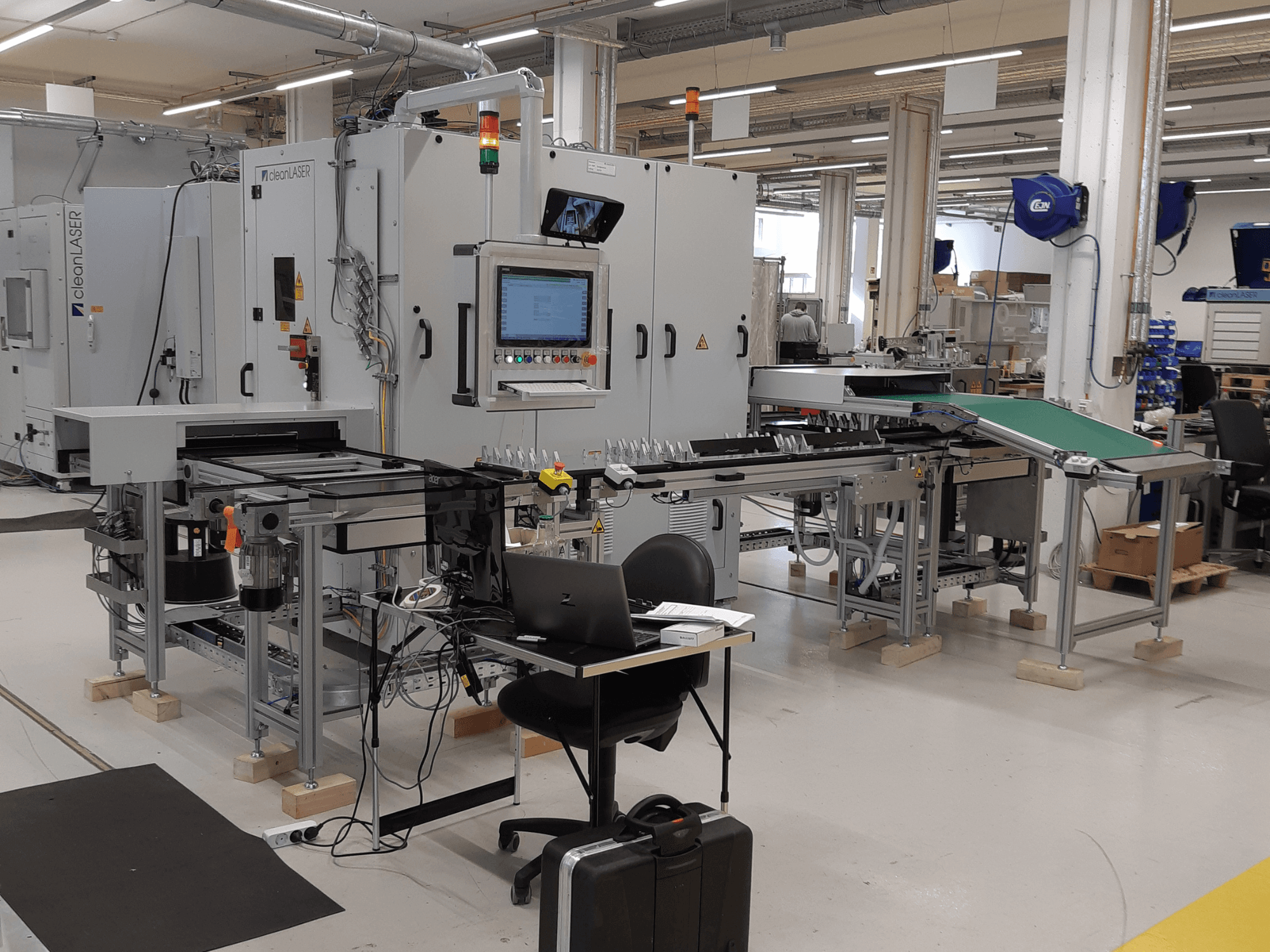 Machine-outil CLEAN LASER clean CELL 3220, vue de face montrant le panneau de commande, le convoyeur et l'aménagement de l'espace de travail dans un environnement industriel.