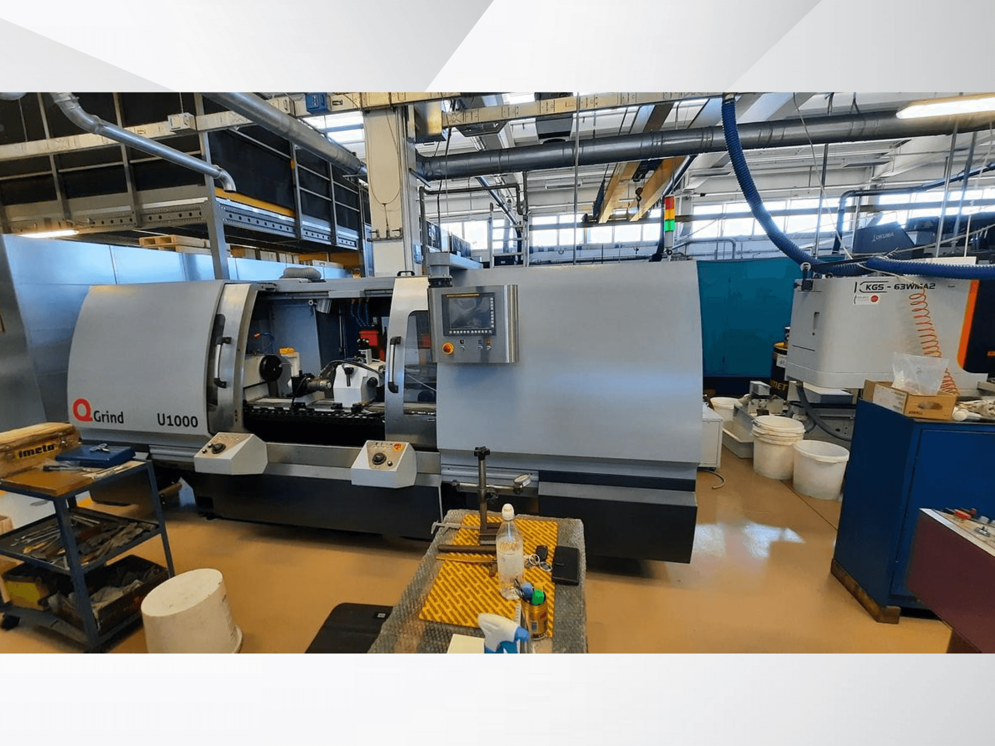 Machine Q-Grind U1000 dans un atelier, présentant une vue de face avec le panneau de commande et la zone de coupe ouverte, entourée d'équipements.