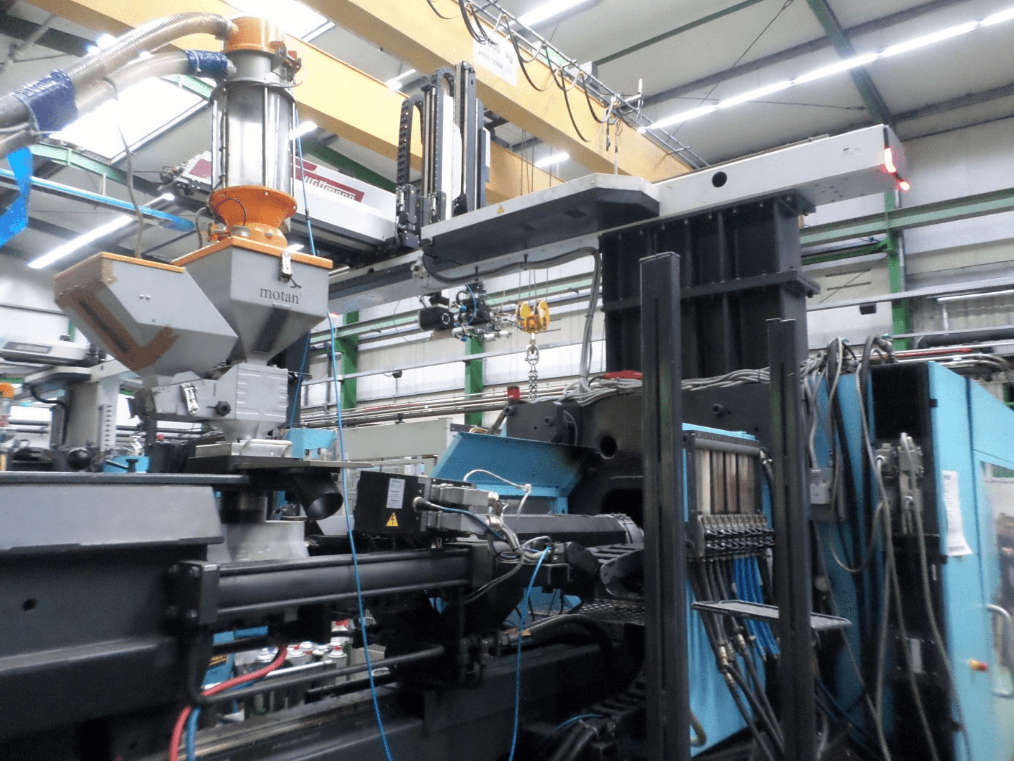 Presse à injection hydraulique DEMAG D 1300, vue latérale, montrant la trémie, l'unité de commande et les raccordements dans un environnement d'usine.