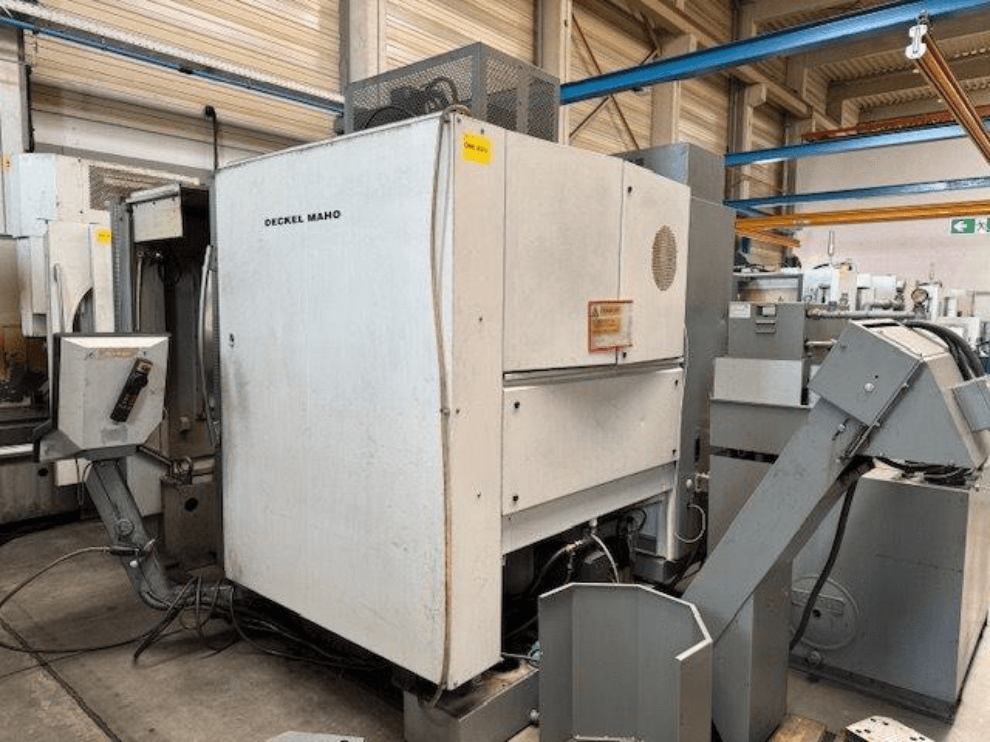 Centre d'usinage vertical DECKEL MAHO DMC 100 V, vue latérale avec panneau de commande et divers accessoires visibles.