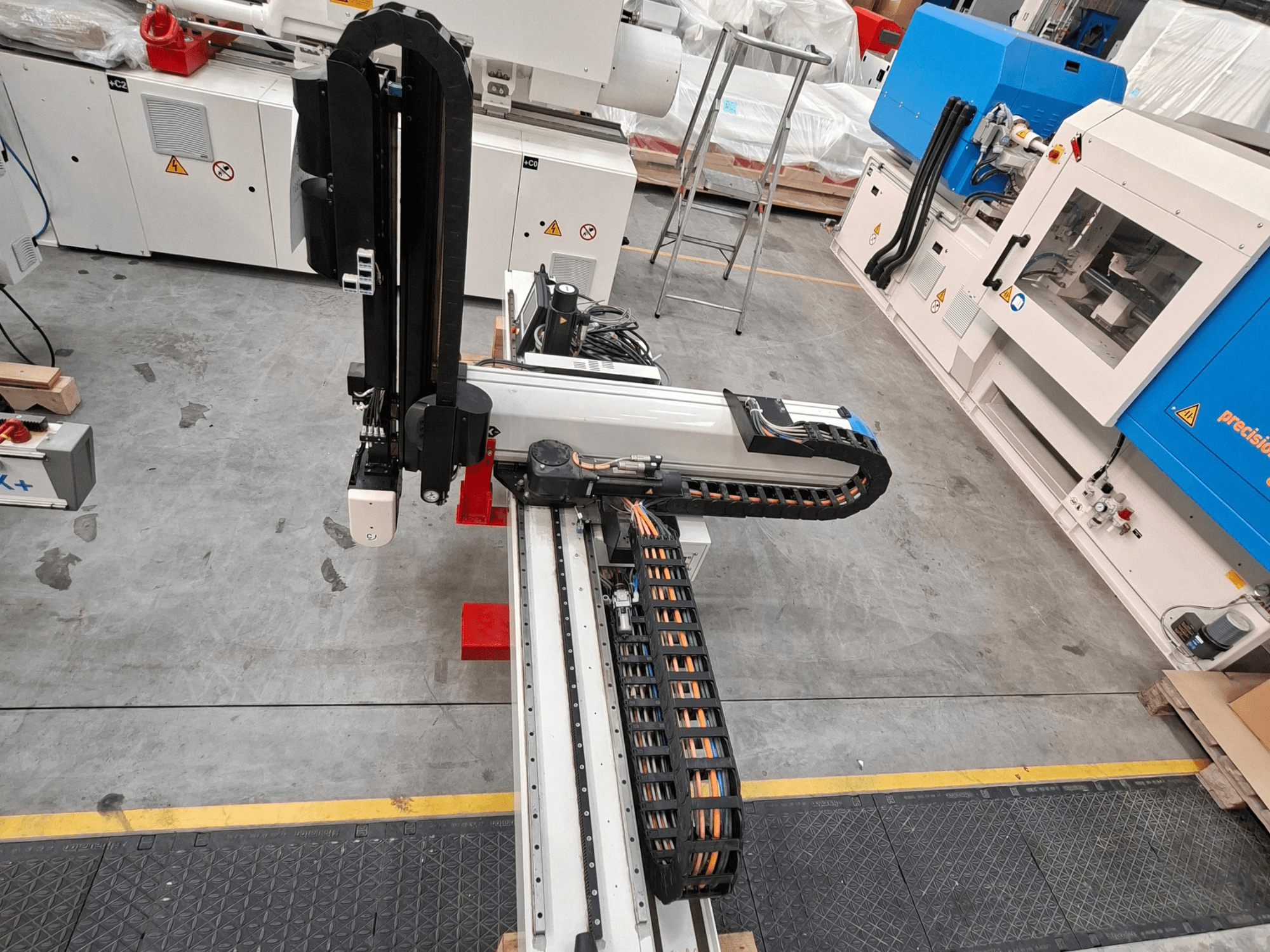 Machine de transformation des matières plastiques Krauss Maffei LRX150-MC5 vue de dessus, mettant en évidence le bras robotisé et le chemin de câbles dans l'atelier.