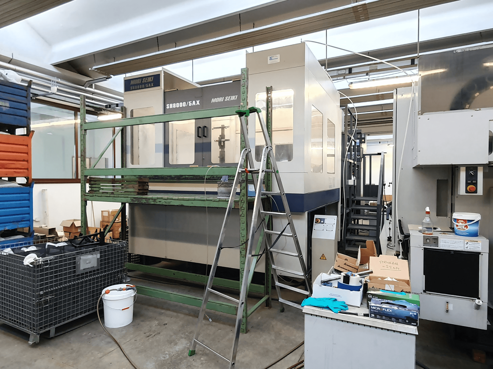 Machine CNC Mori Seiki SH-8000/5AX dans un atelier, vue de face, avec des outils d'atelier et des boîtes de rangement à proximité.