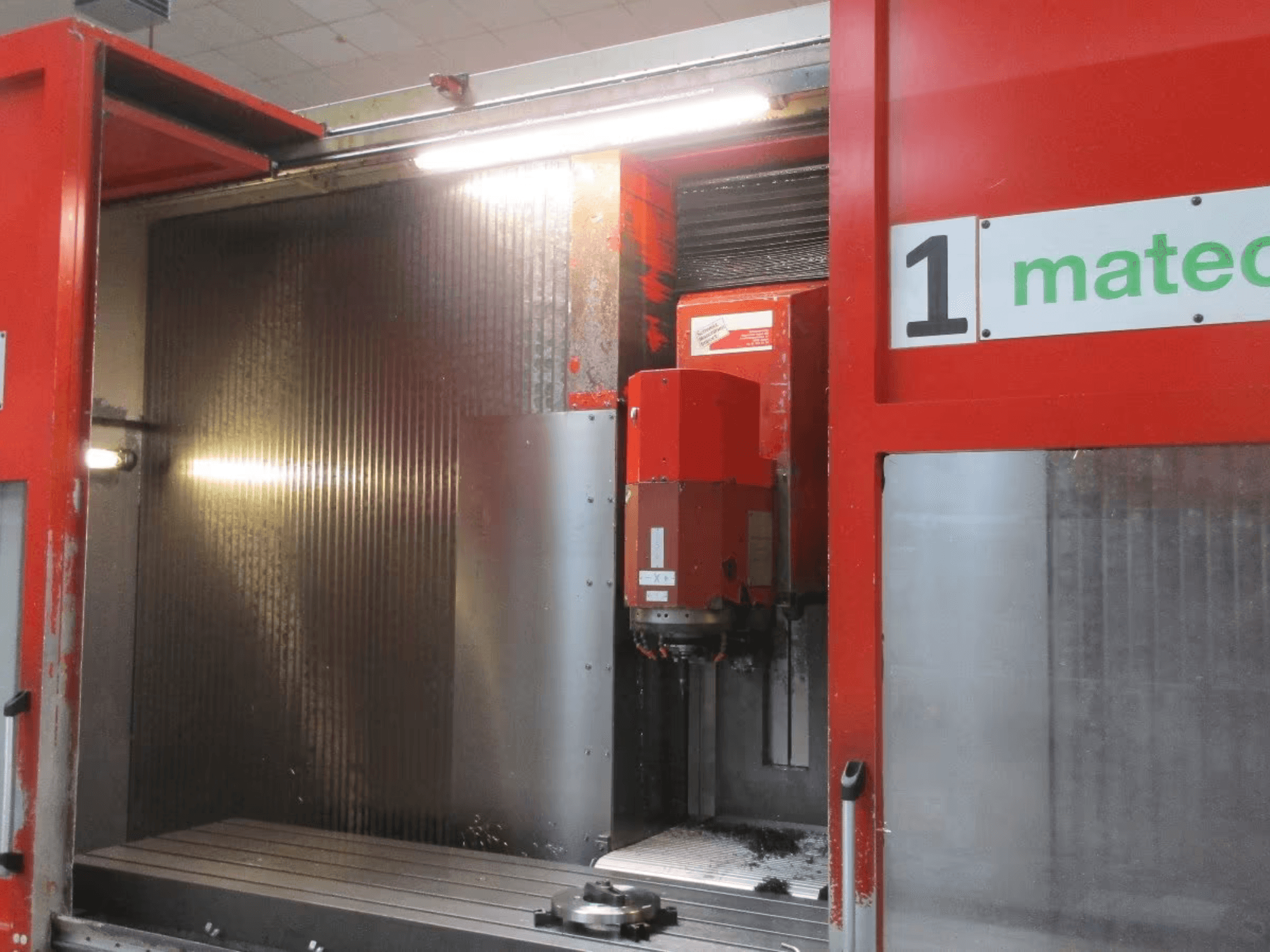 Vue de face du centre d'usinage vertical CNC Matec 30 HV avec l'outil de coupe visible, la surface du métal et les détails de l'intérieur de la machine.