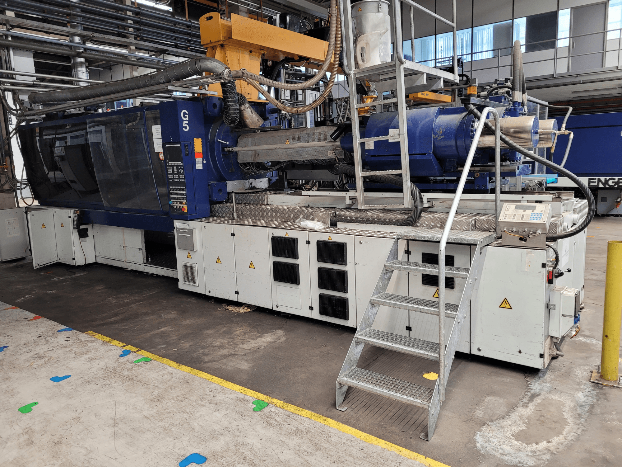 Machine de moulage par injection G5, vue de côté, avec le panneau de commande, l'escabeau et le plan de travail en acier inoxydable visibles.