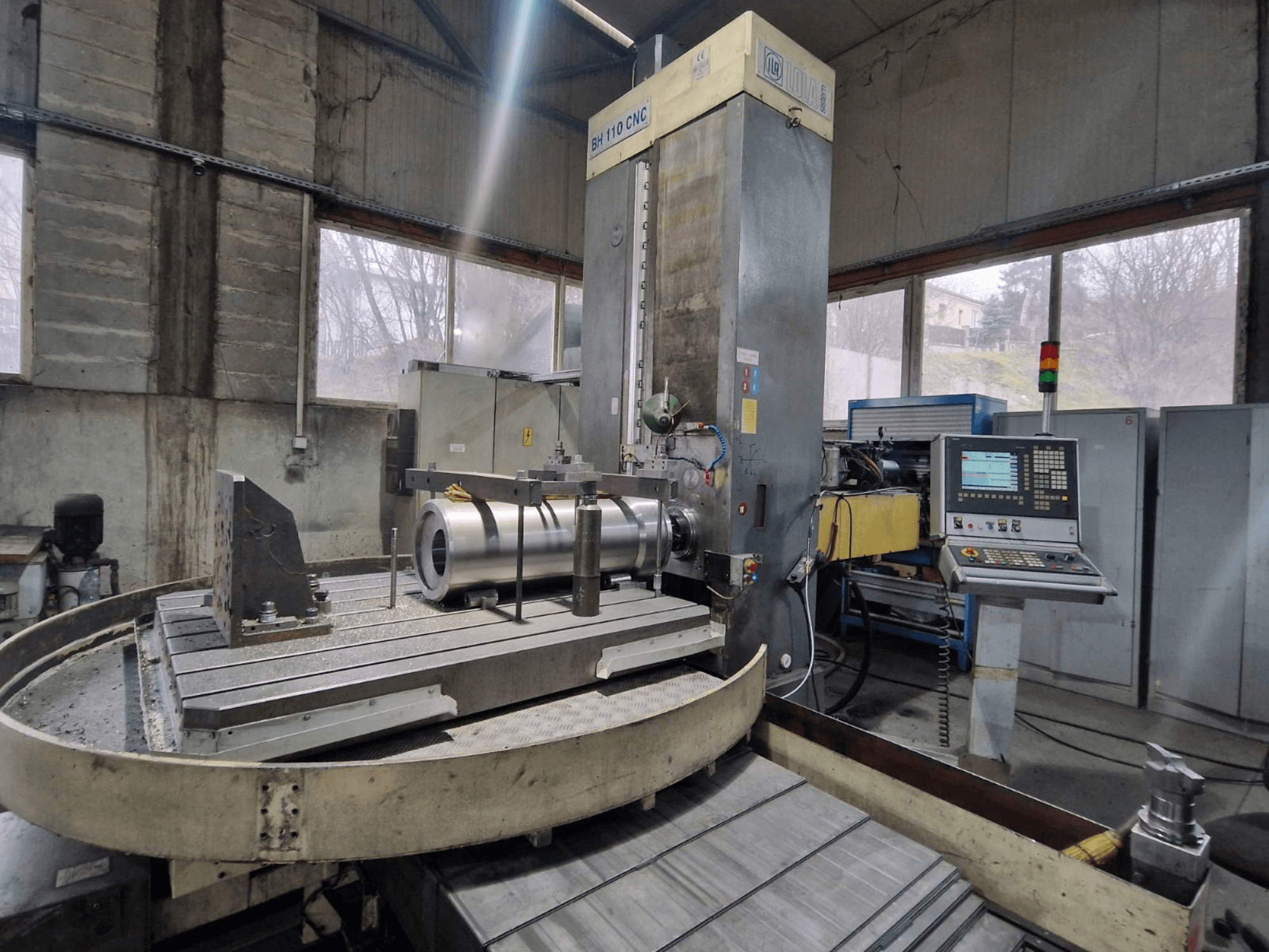 Aléseuse CNC LOLA BH 110 dans un atelier, vue de face, avec pièce métallique et panneau de commande.