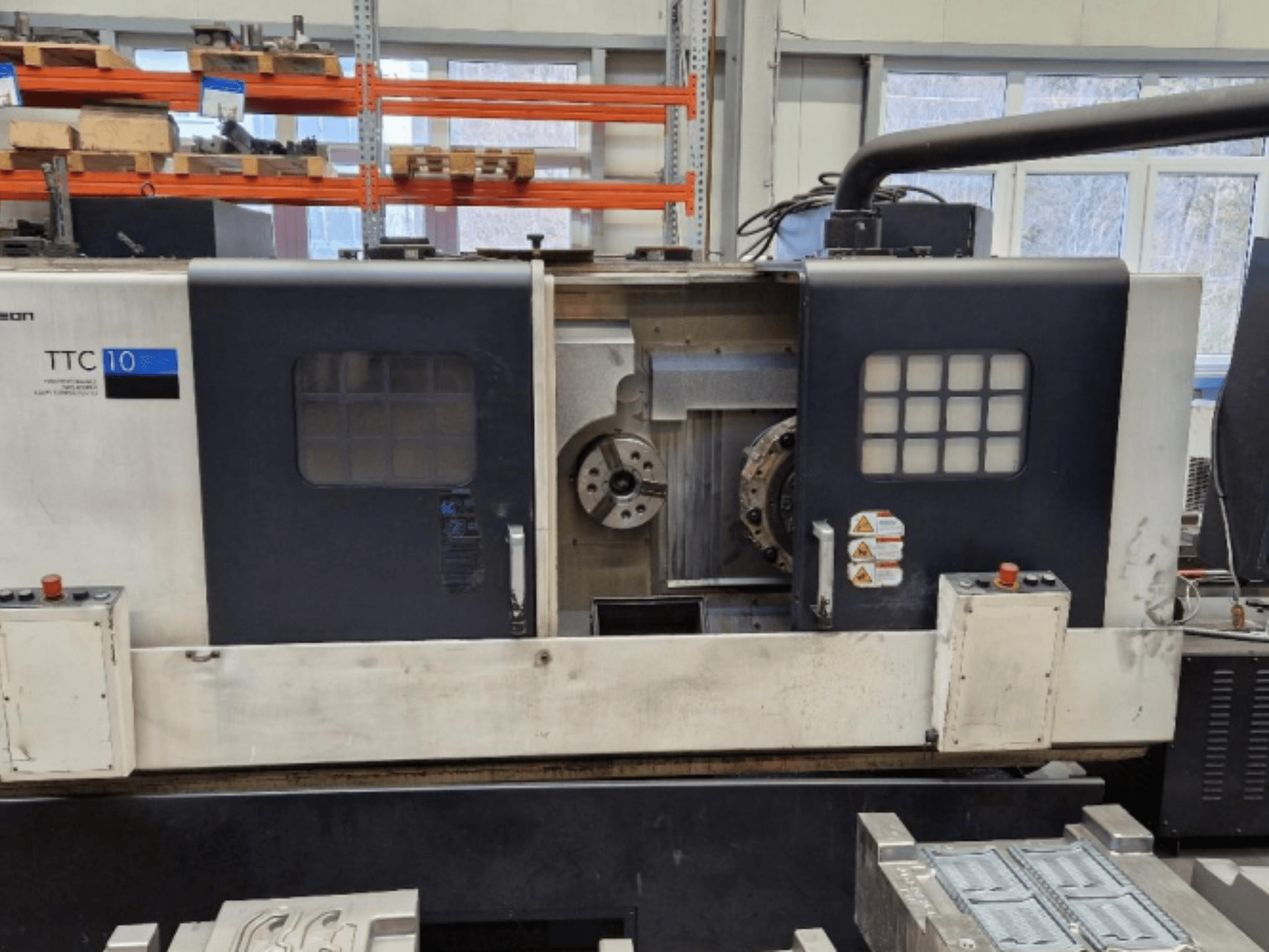 Vue de face du tour TTC 10, montrant le panneau de commande, les mandrins visibles et l'espace de travail avec des pièces métalliques.