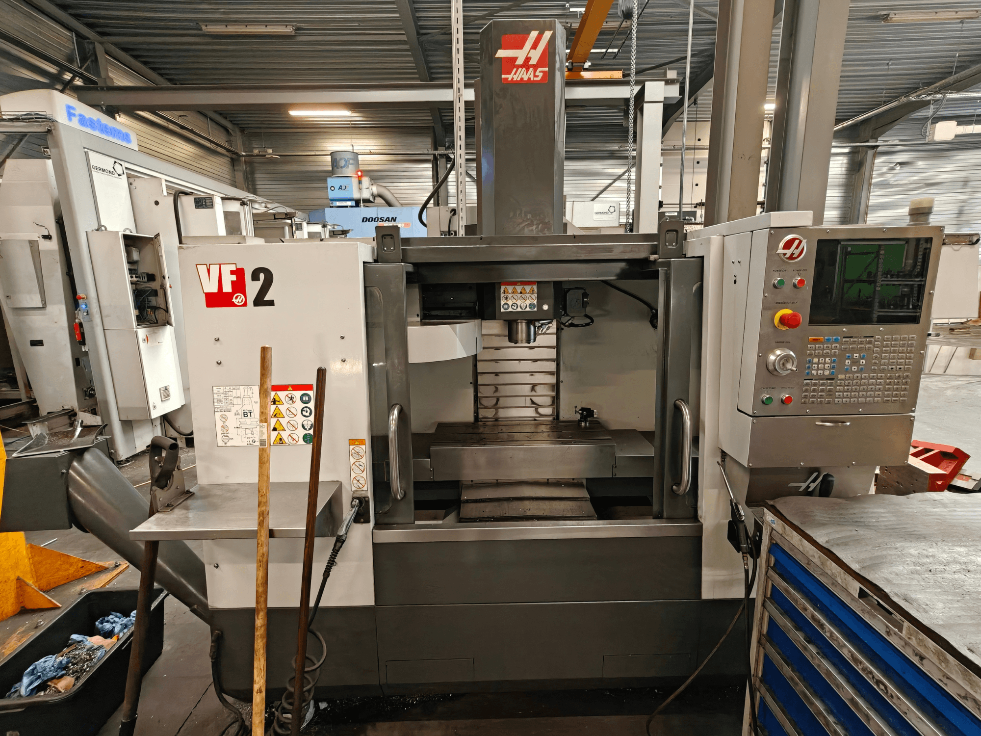 Centre d'usinage vertical HAAS VF-2, vue de face, mettant en évidence les commandes, la broche et la table de travail dans un environnement d'atelier.