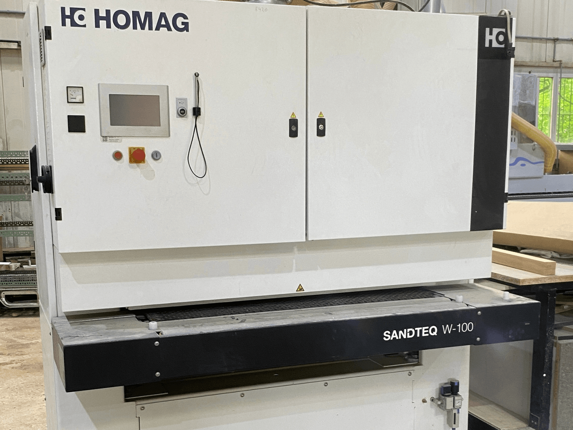 Ponceuse à bande HOMAG SANDTEQ W-100 dans un atelier, montrant le panneau de commande, la prise d'aspiration et la zone de la bande abrasive. Vue de face.
