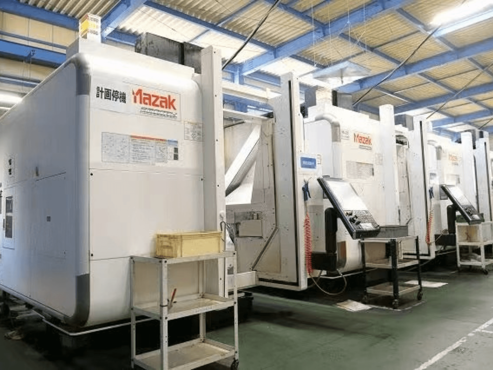 Machines CNC Mazak dans une usine, vue latérale montrant des panneaux de contrôle et des étiquettes sur des corps blancs.