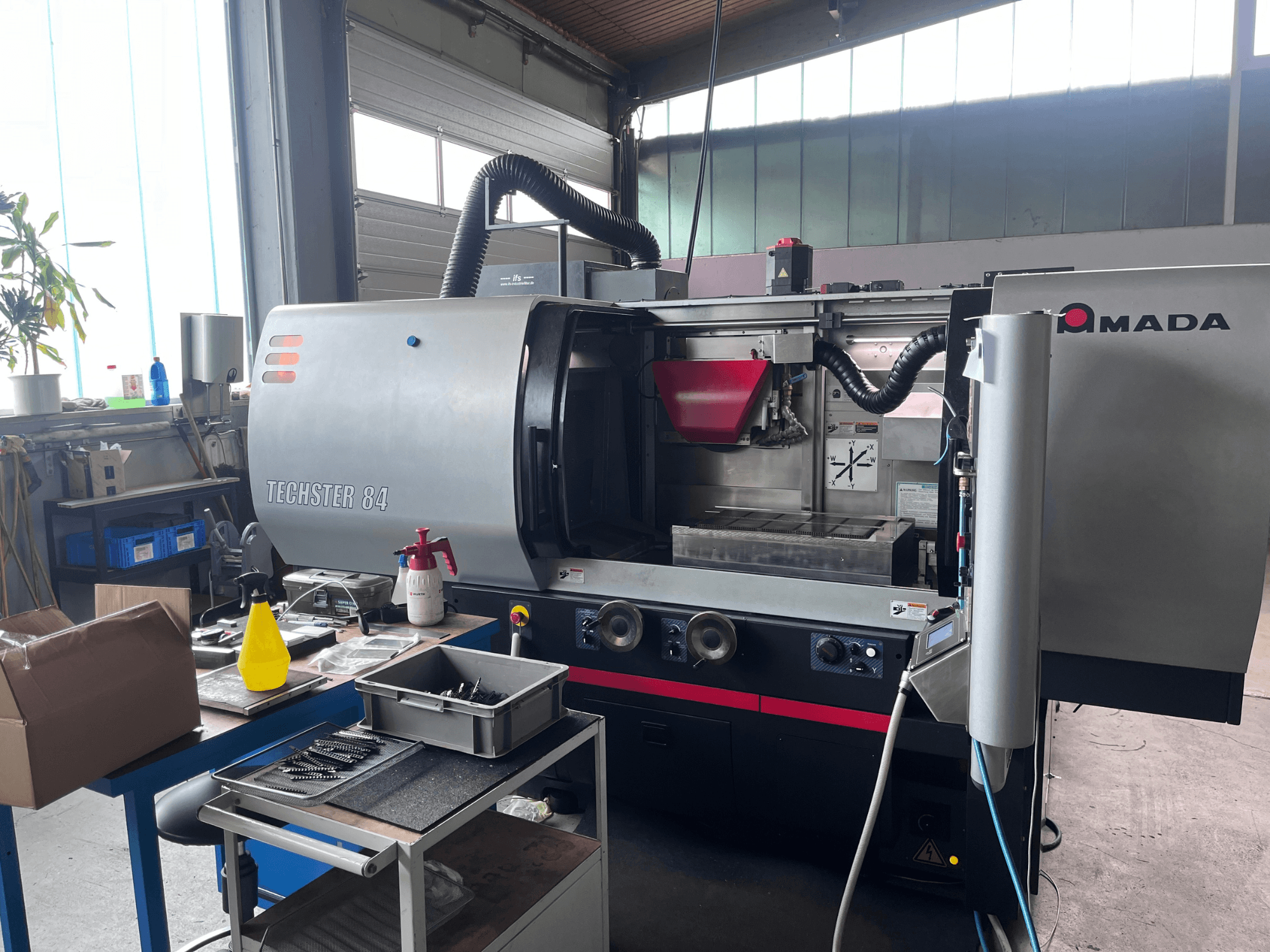 Rectifieuse plane AMADA Techster 84 dans un atelier, vue de face montrant les commandes de fonctionnement et la trémie rouge.
