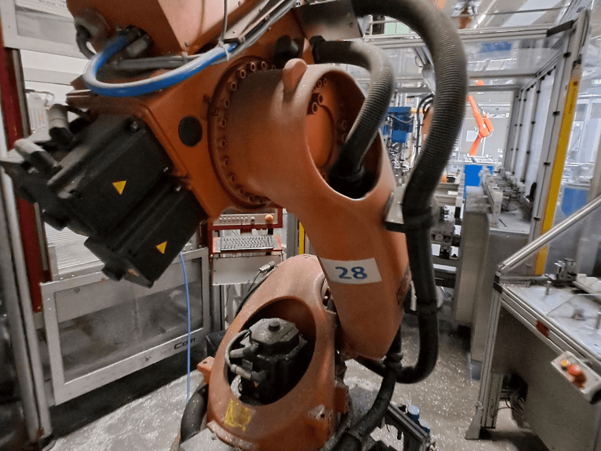 Gros plan sur le bras robotisé KUKA KR30-3, avec son corps orange portant le numéro 28, montrant les moteurs et le câblage vus de profil.