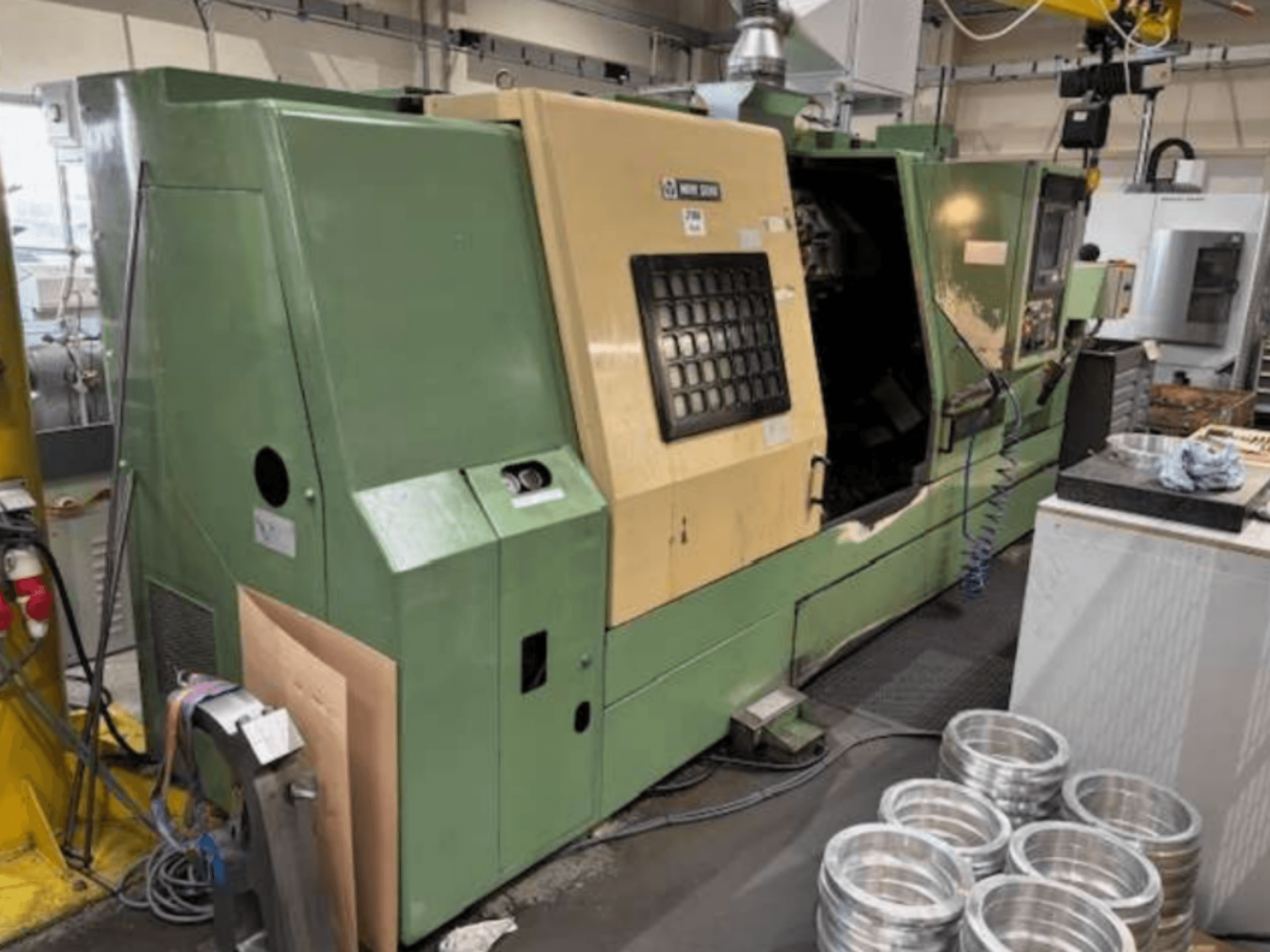 Tour CNC vert de Mazak, vu de face, présentant un panneau de commande et des pièces d'aluminium usinées sur une table de travail.