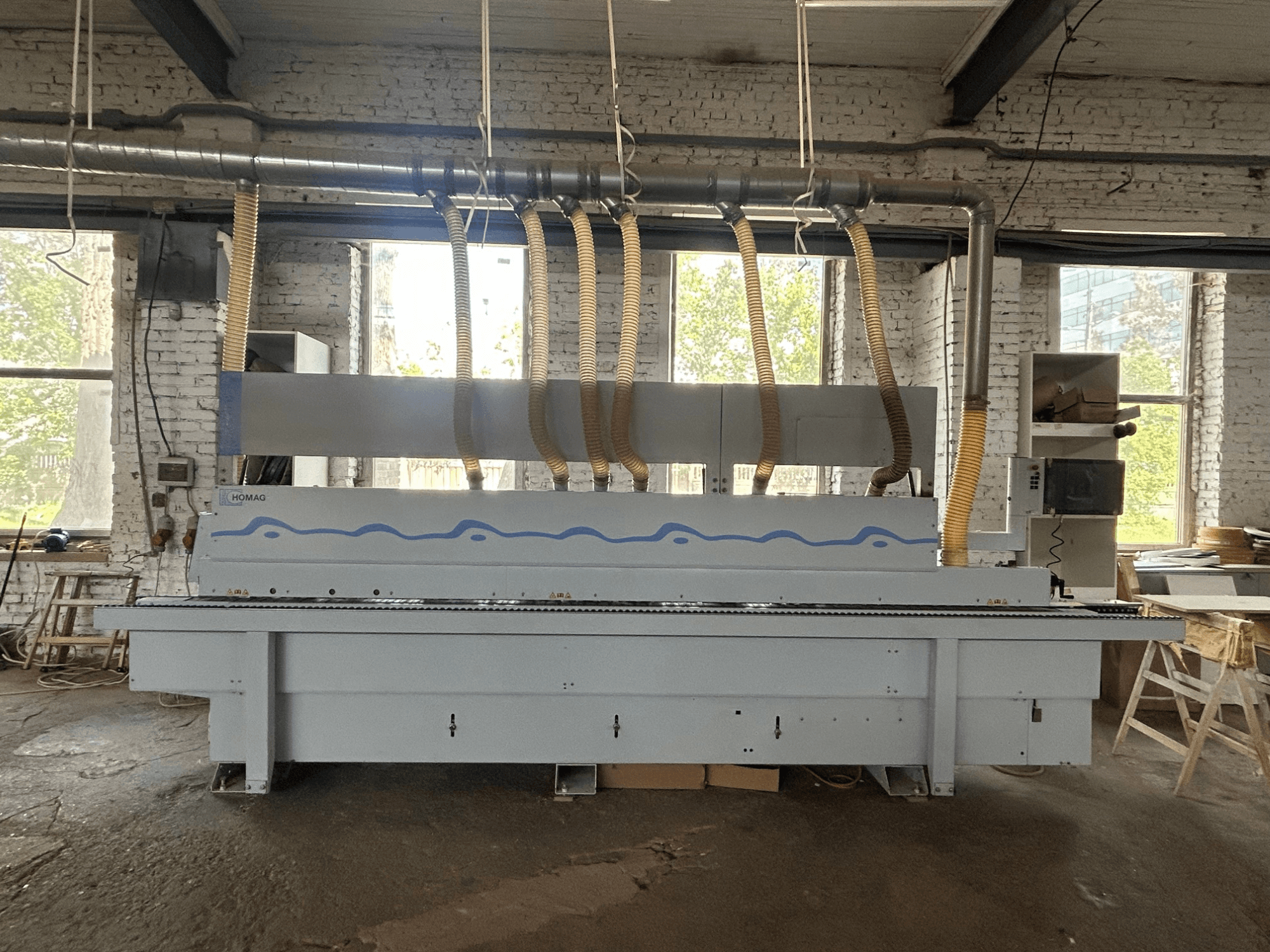 Vue de face de la plaqueuse de chants HOMAG Optimat KDF 440 C, montrant une machine de grande taille équipée de tuyaux d'aspiration et d'un panneau de commande.