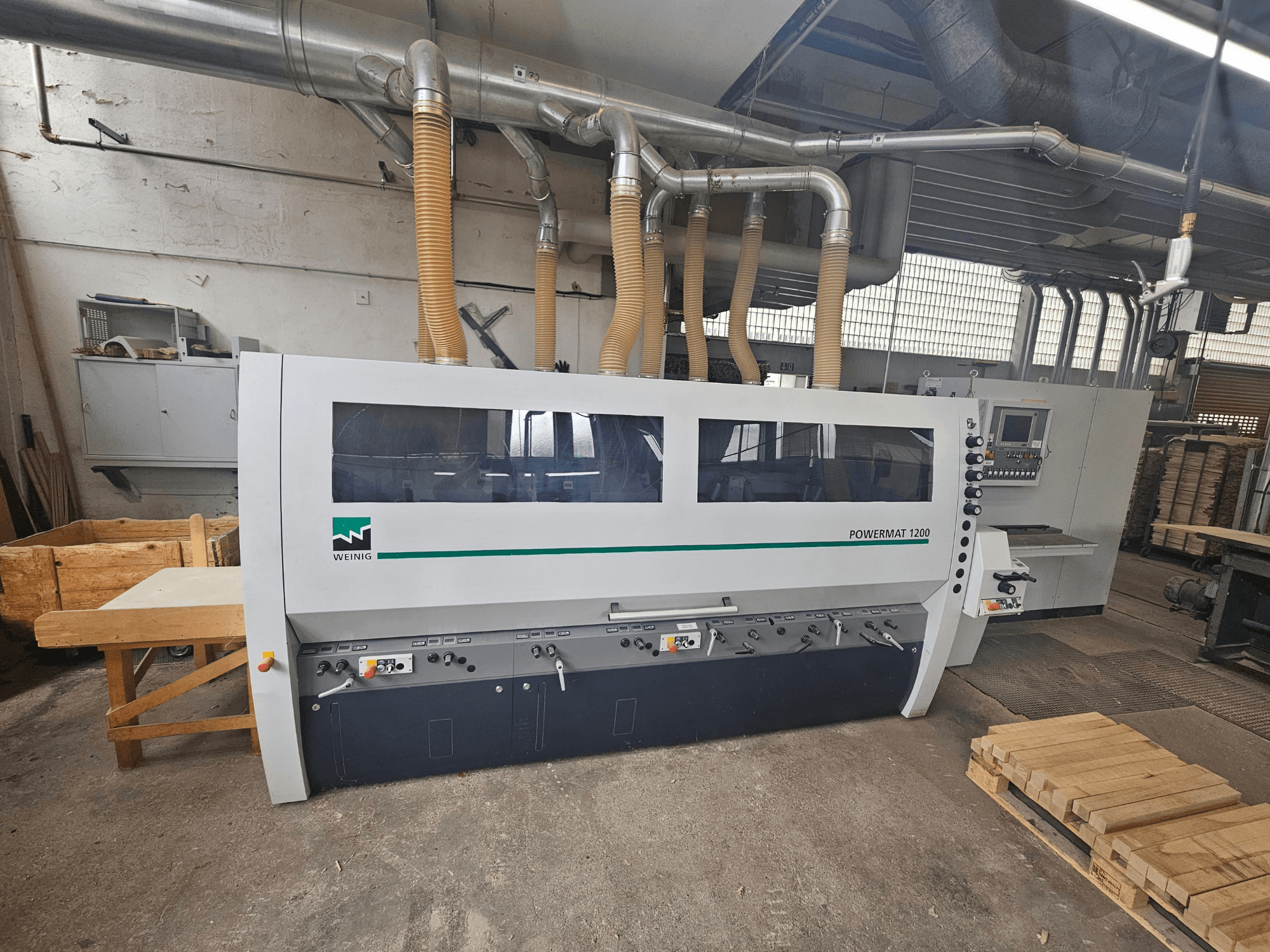 Machine à bois Weinig Powermat 1200, vue de face, avec panneau de commande et piles de bois dans un atelier.