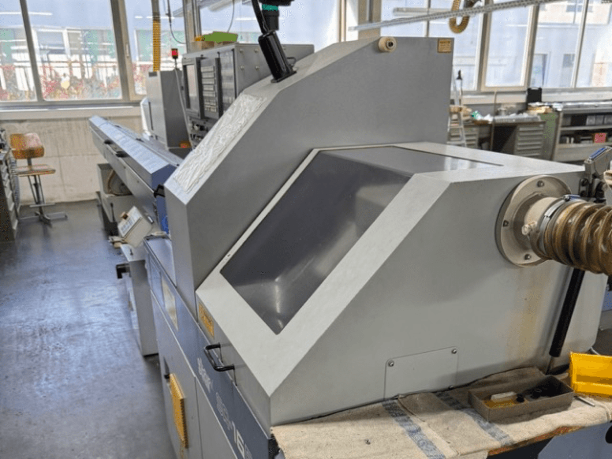 Machine industrielle grise vue de côté, avec un grand panneau incliné, des boutons de commande et un tuyau d'arrosage.