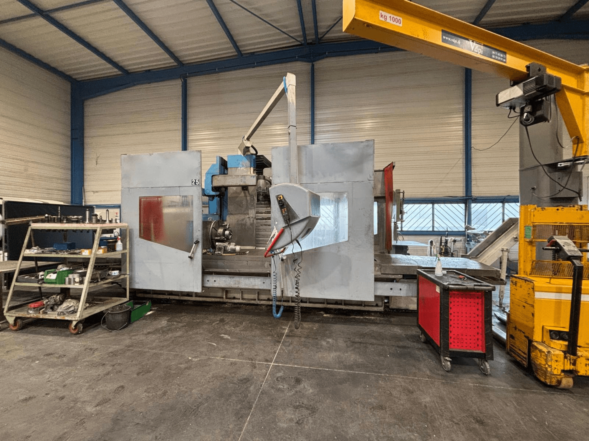 Fraiseuse CNC vue de côté dans un atelier ; outils et étagères de rangement visibles. Marque et modèle non spécifiés.