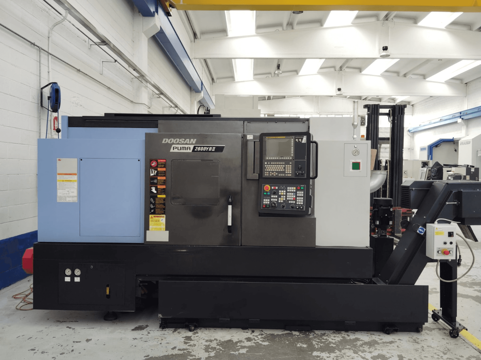 Vue avant du tour horizontal DOOSAN Puma 2600YB II avec panneau de commande et étiquettes de sécurité visibles.