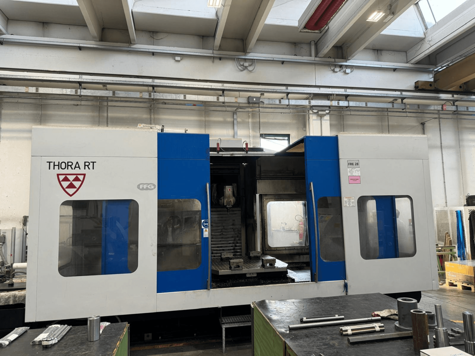 Machine CNC THORA RT vue de face, avec un extérieur bleu et blanc, des fenêtres transparentes et des outils montés.