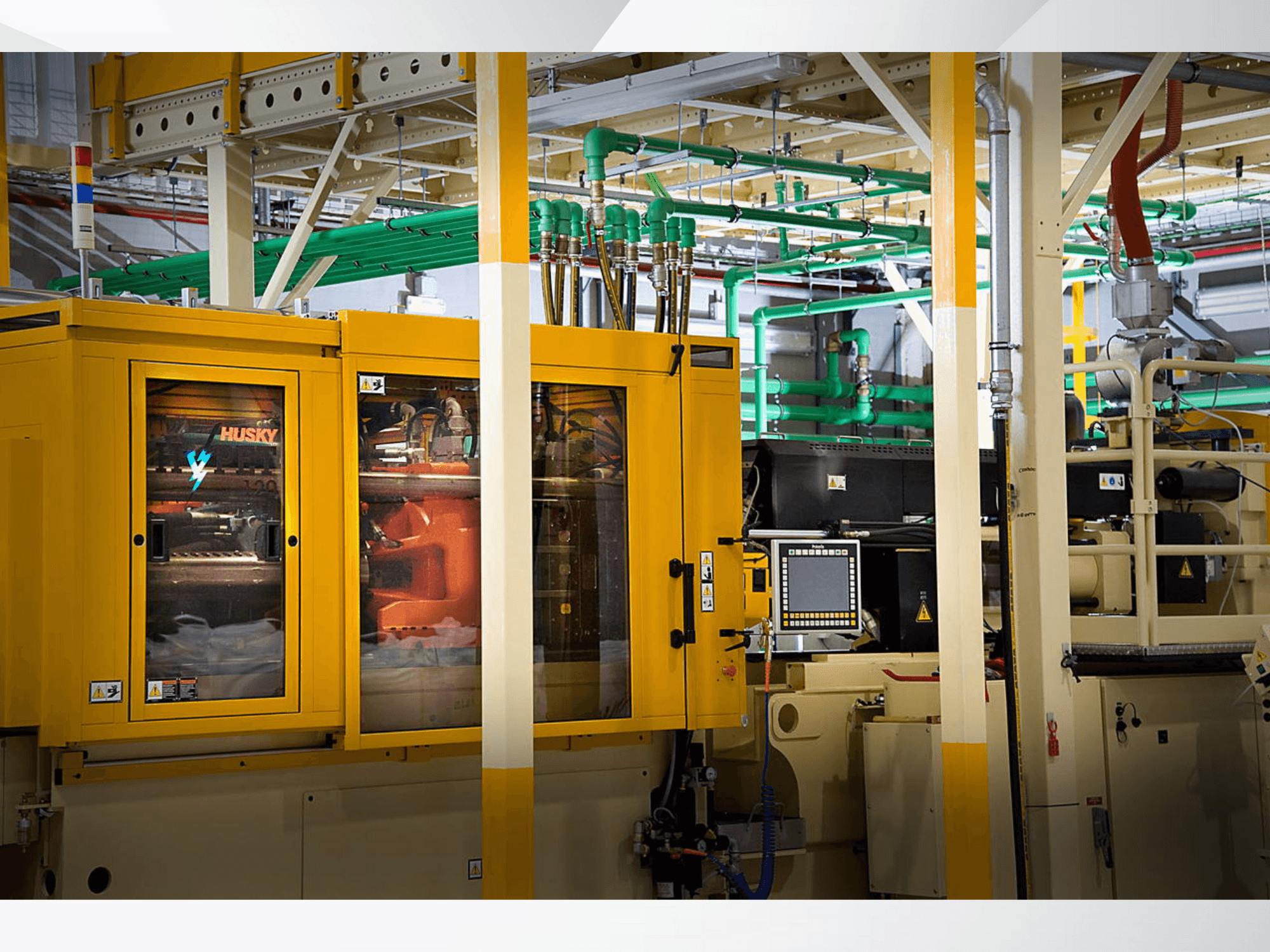 Machine industrielle Husky en jaune, vue de face présentant le panneau de commande et les mécanismes internes sur fond d'usine.